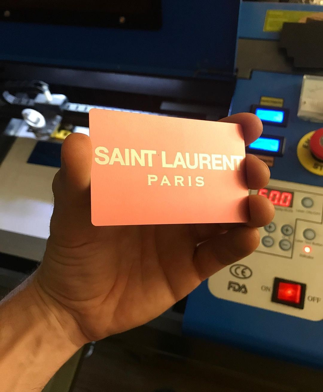 Hand holding a laser engraved rose gold & silver metal business card with custom business branding in front of a cnc machine