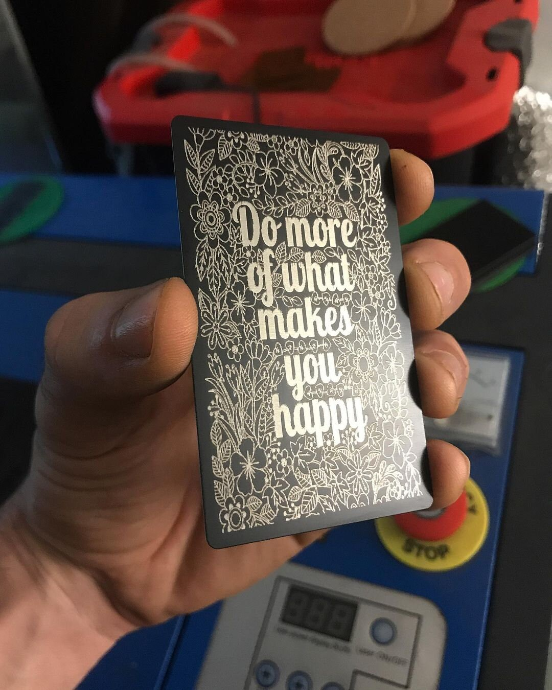 Hand holding a laser engraved metal keepsake card with motivational quote in a workshop setting