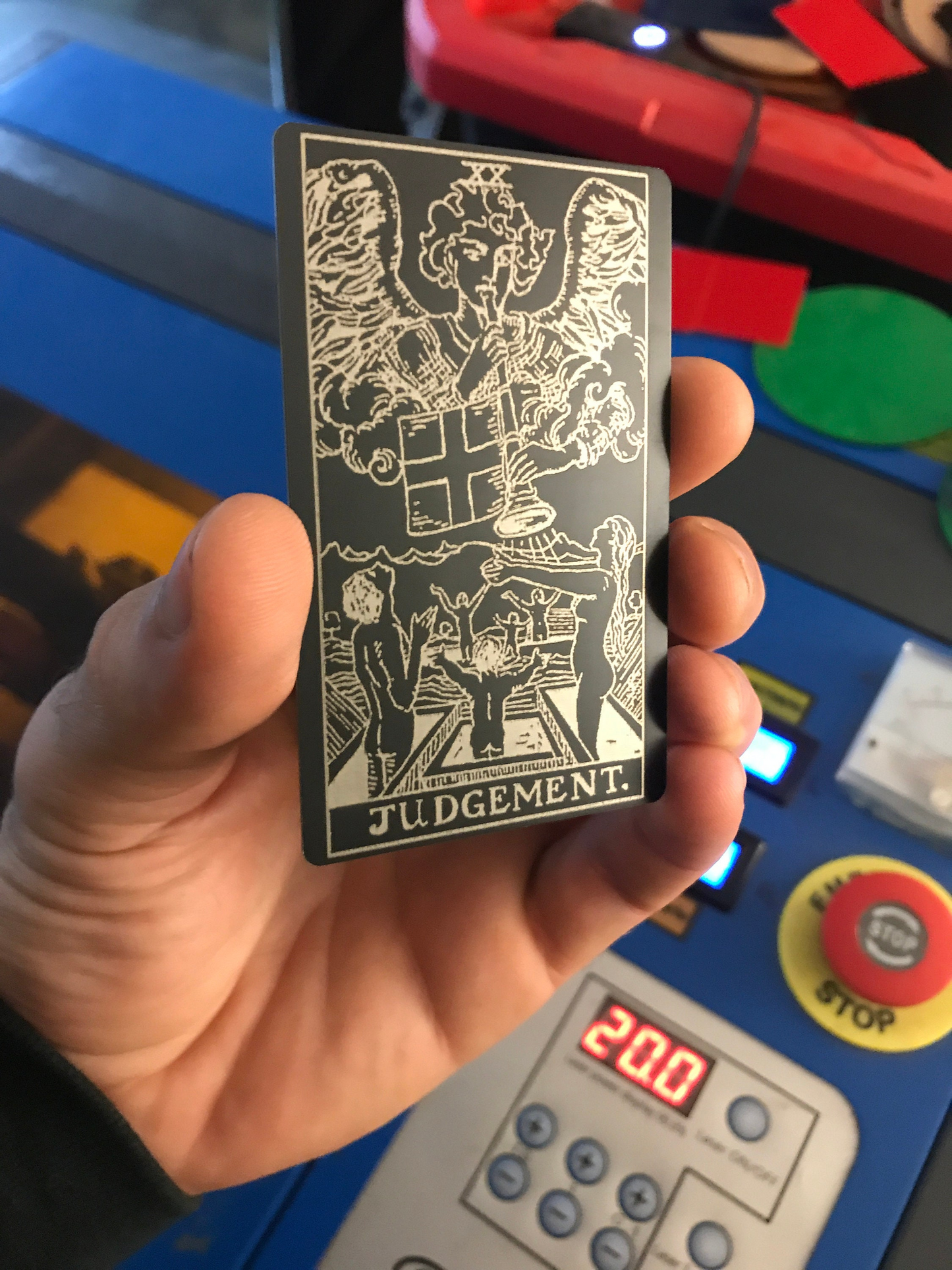 Hand holding a metal tarot card titled 'Judgment' in front of a colorful background.