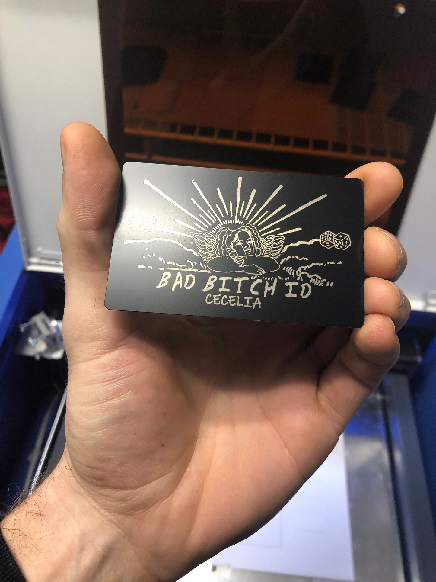 Hand holding a black card with white text and design, against a blurred background.