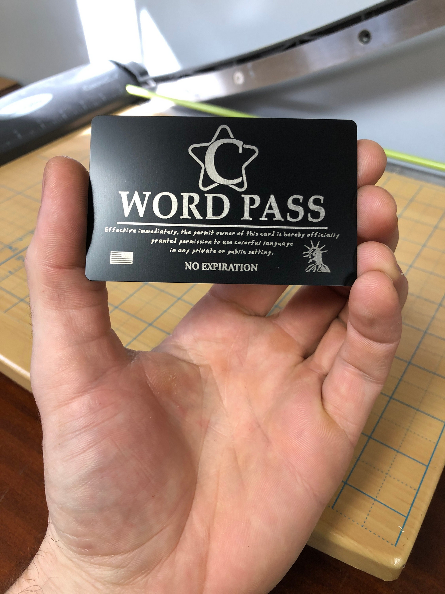 Hand holding a black/silver metal card with 'C WORD PASS' text and branding against a blurred background