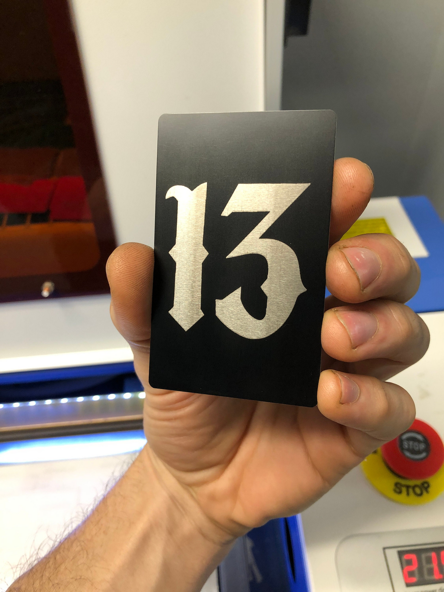 Hand holding a metal wallet insert card with the number 13 on it in front of a blurred background.