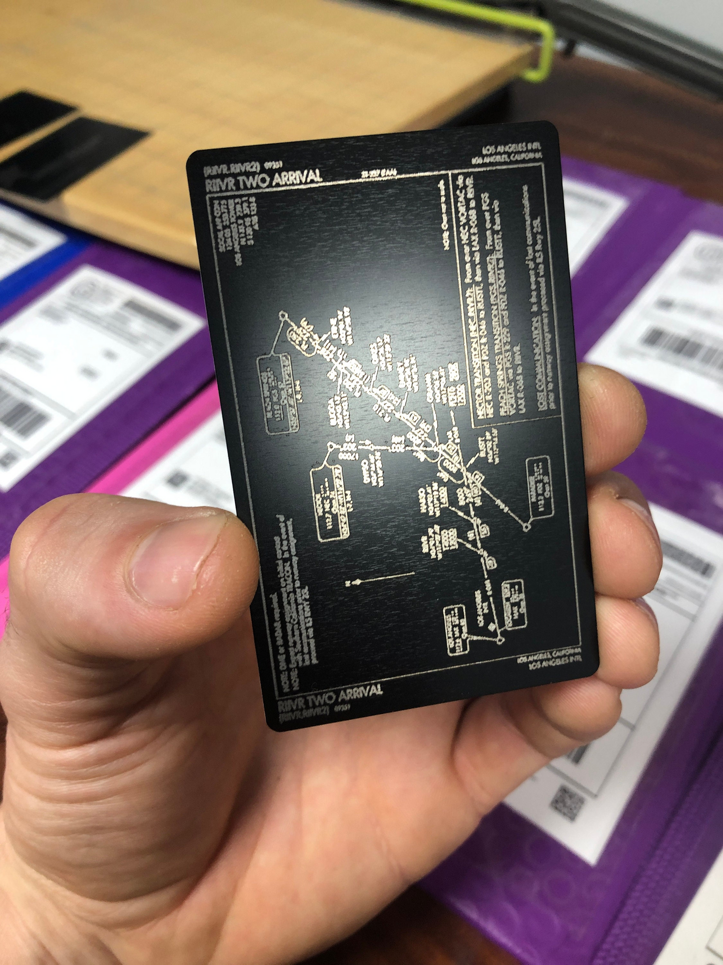 Hand holding a black card with technical drawings and text against a blurred background