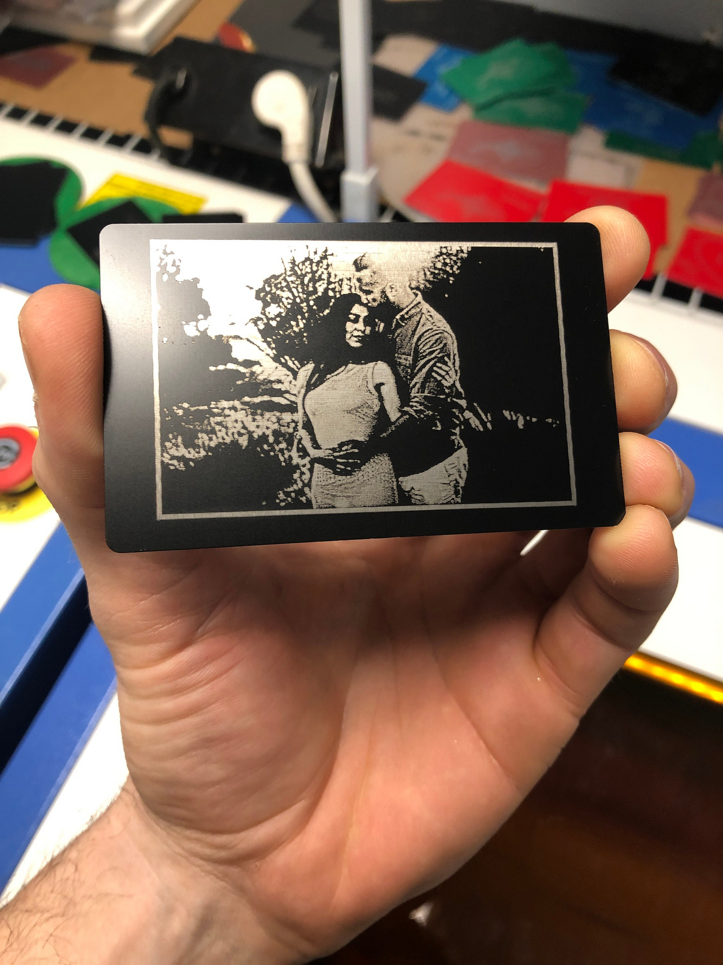 Hand holding a small engraved metal card with a black and white image of a couple.