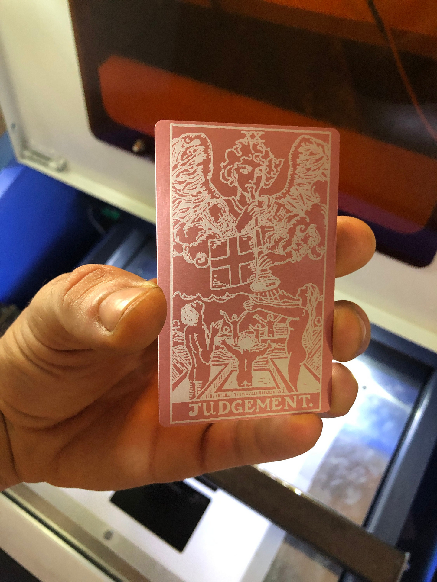 Hand holding a laser engraved rose gold/silver metal keepsake card with white designs and text, blurred background