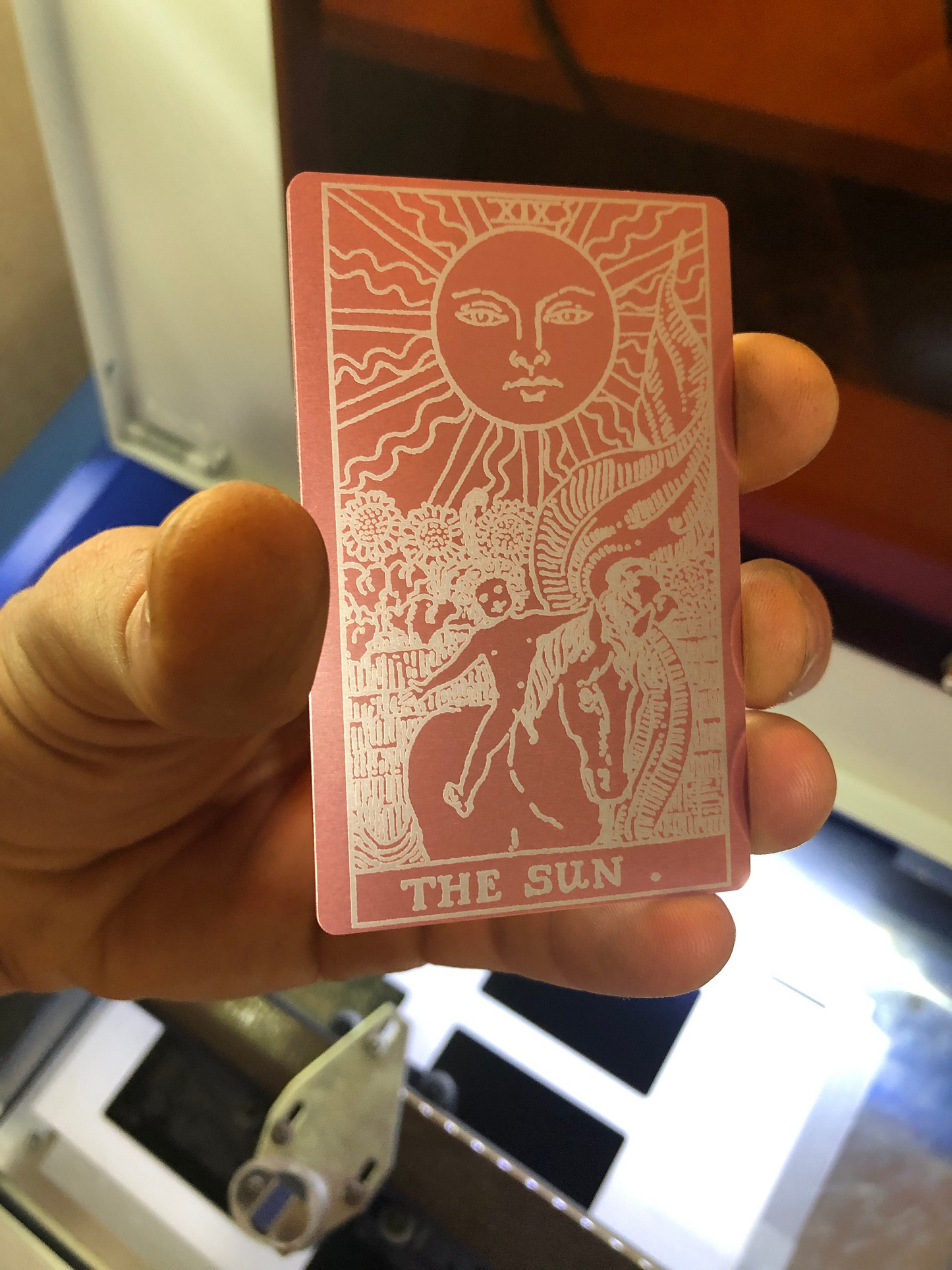 Rose gold/silver card with a sun design and 'The Sun' tarot design held by a hand.