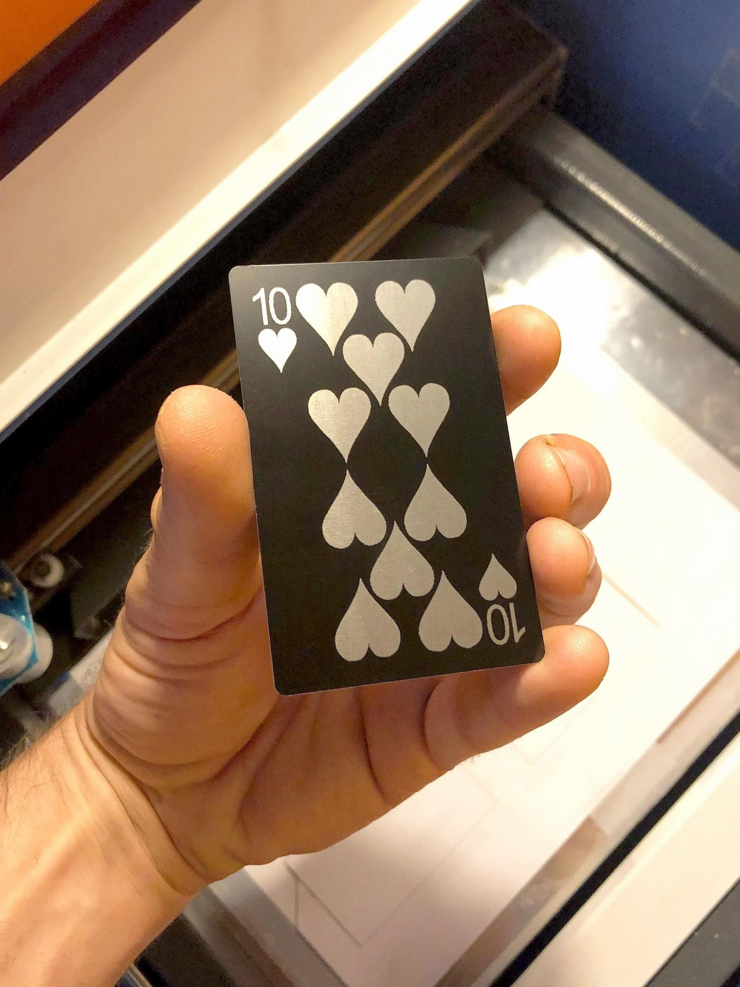 Hand holding a black and silver laser engraved metal playing card with ten of hearts on front