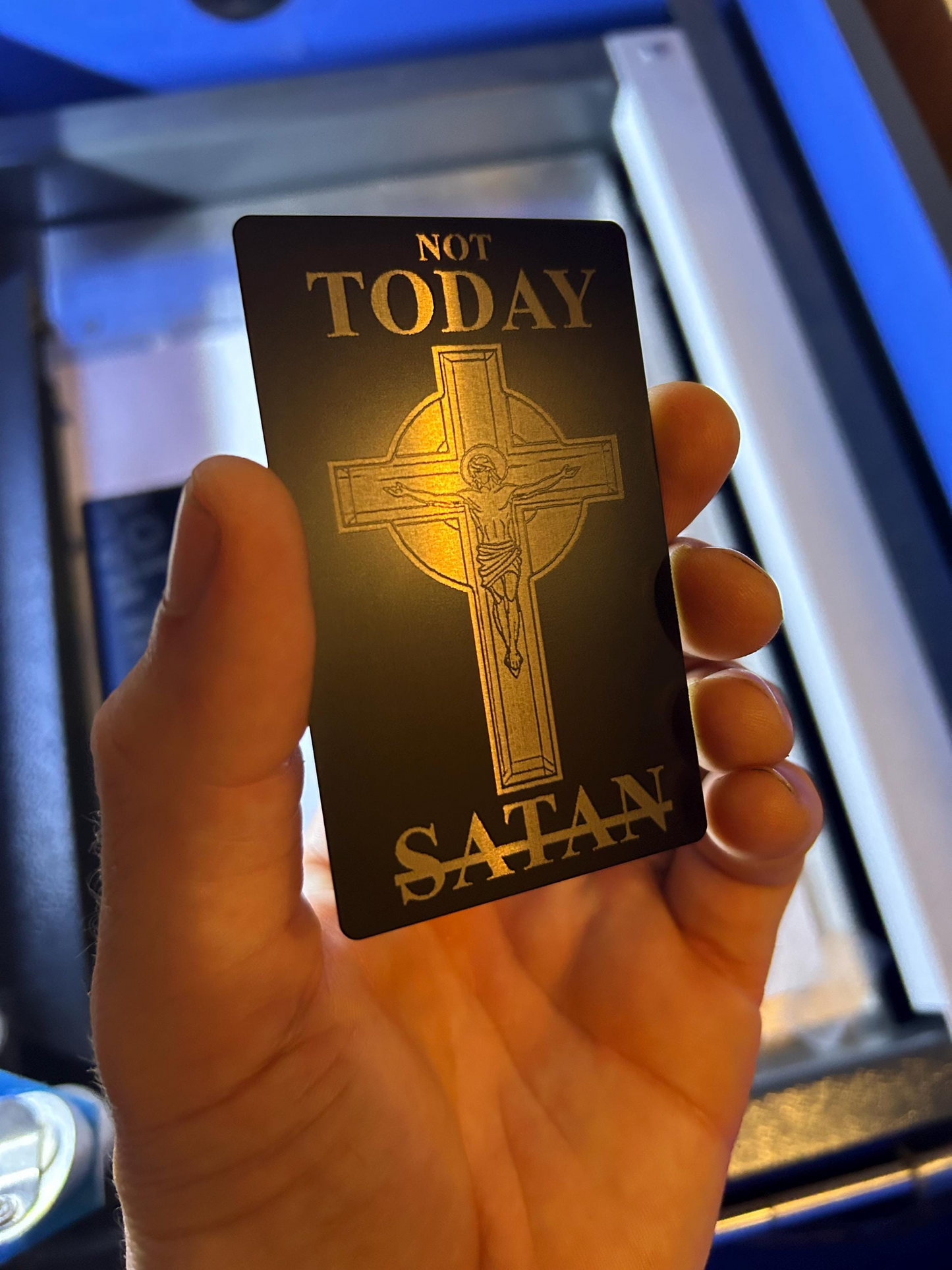 Hand holding a laser engraved metal placard with 'Not Today Satan' text and cross design.
