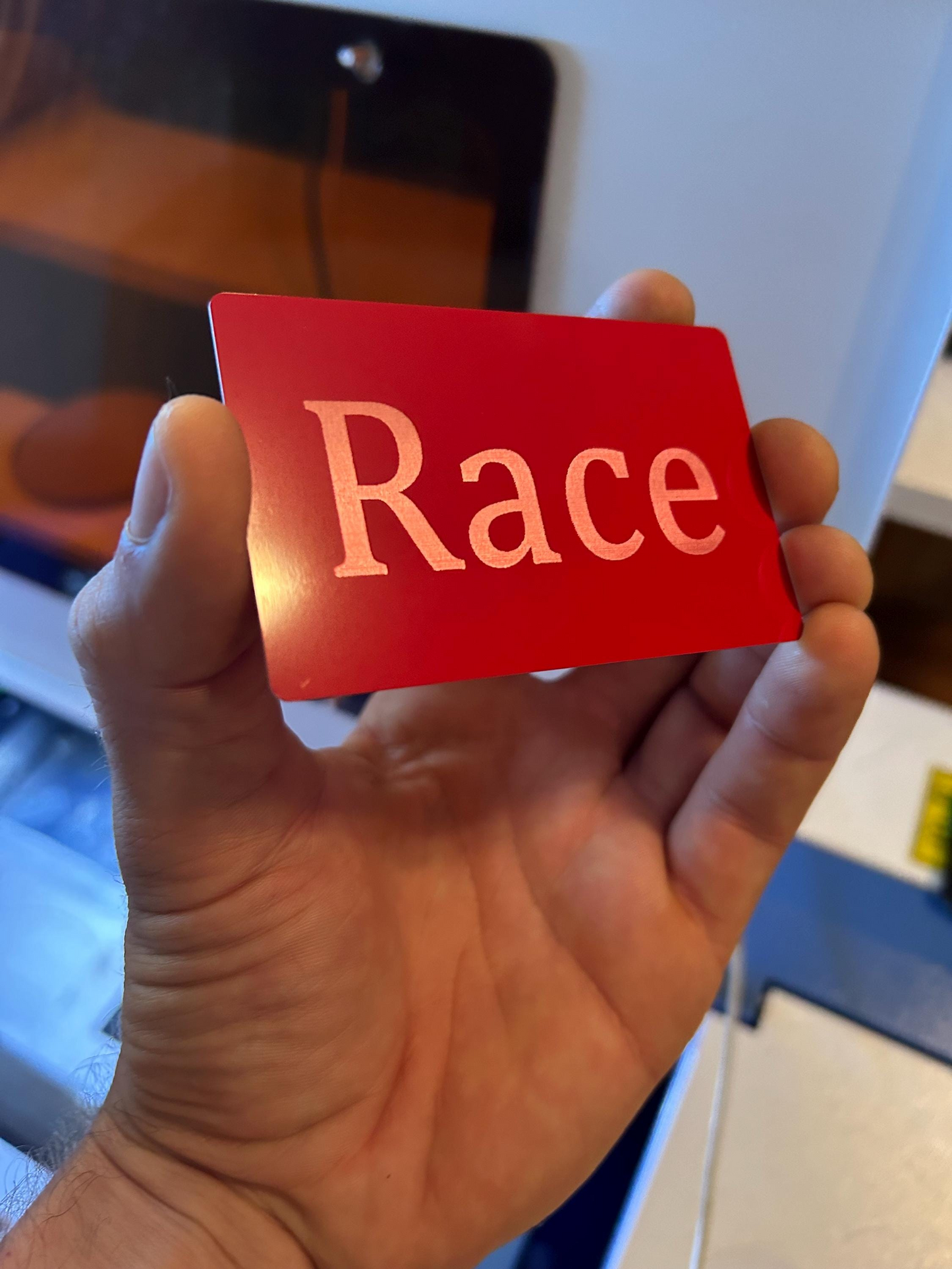 Hand holding a red/silver laser engraved card with 'Race' engraved on it as a joke