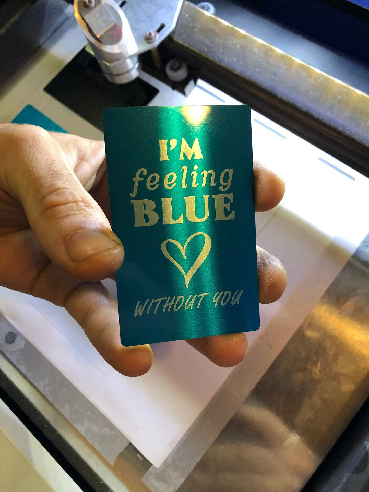 Hand holding a blue/silver metal keepsake i miss you card with engraved text and a heart symbol.