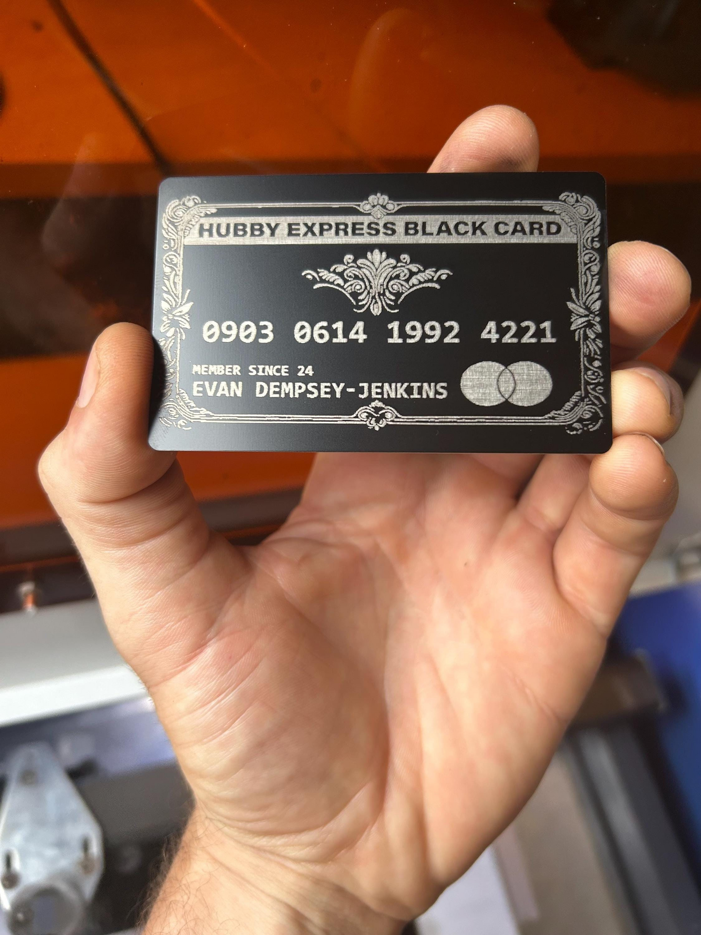 Hand holding a black metal card with 'HUBBY EXPRESS BLACK CARD' text and numbers.
