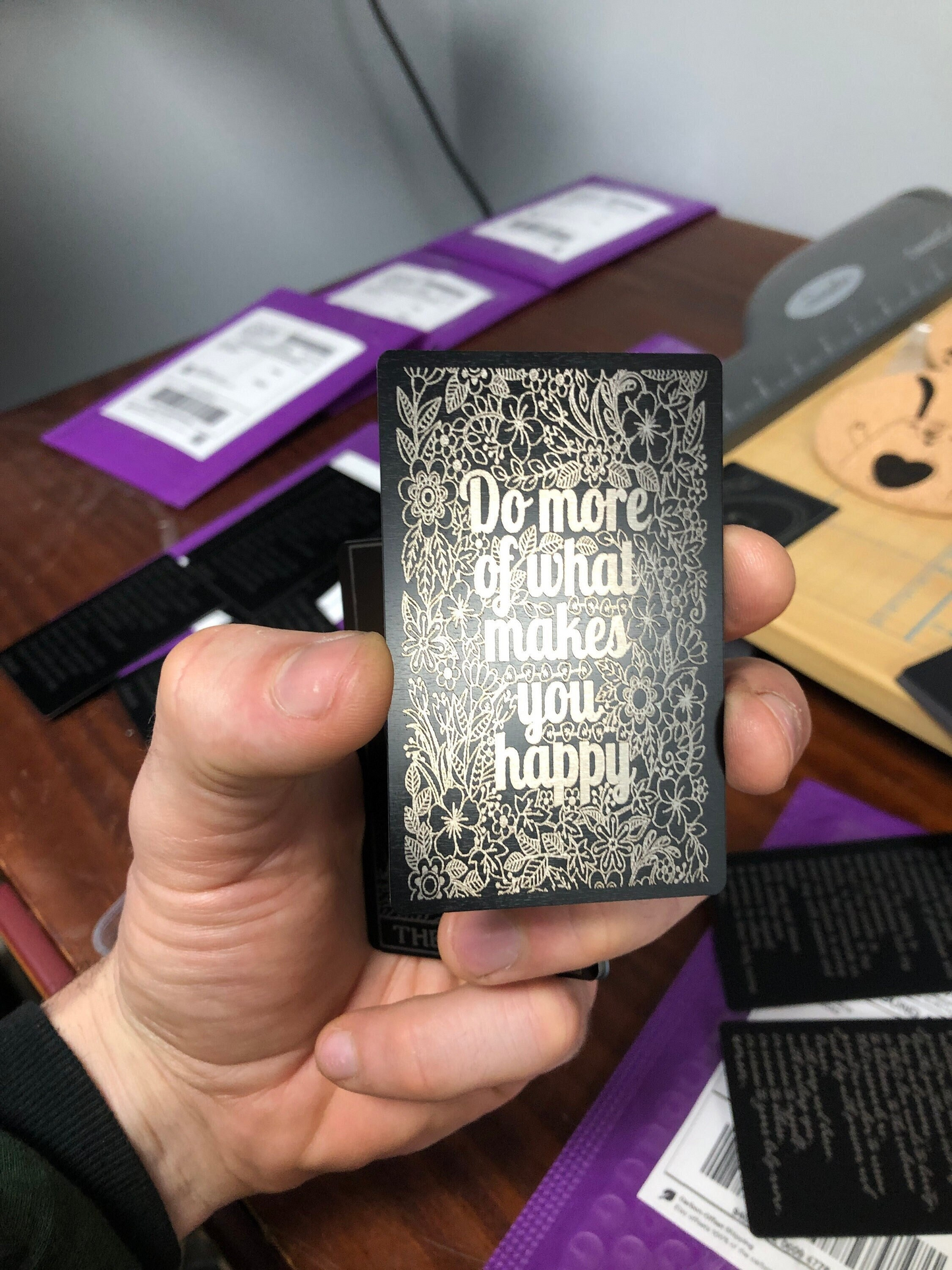 Hand holding a black anodized aluminum metal card with silver laser engraved text on a blurred background