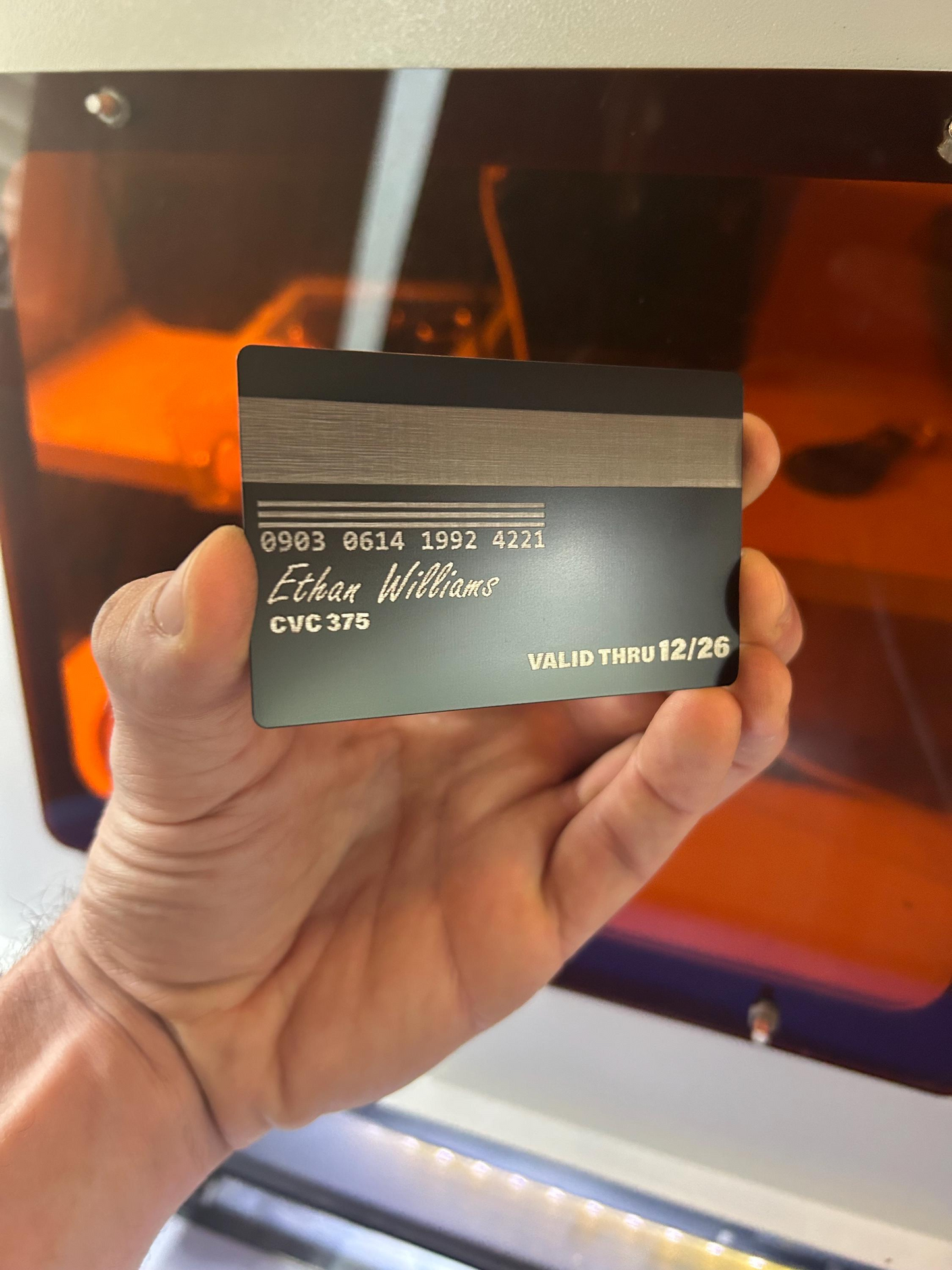 Hand holding a black and silver card with text and faux magnetic strip against a blurred background
