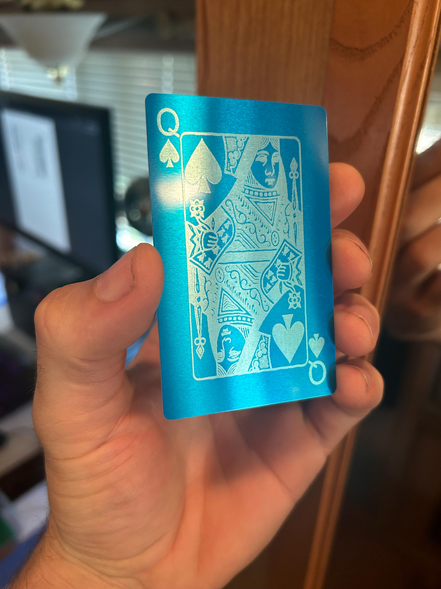 Hand holding a blue/silver metal playing card with a queen of spades design.