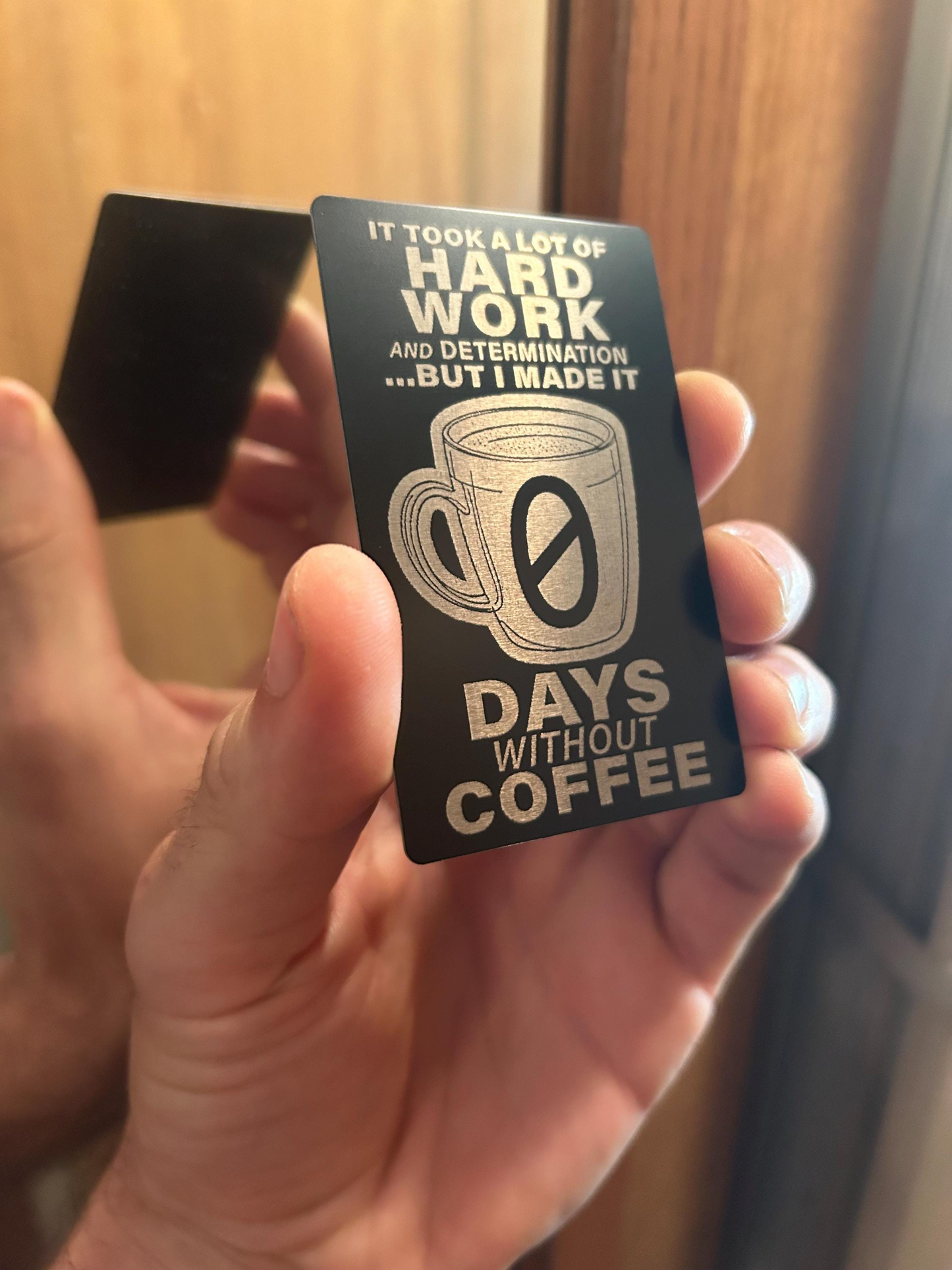 Card with '0 Days Without Coffee' text held by a person against a neutral background