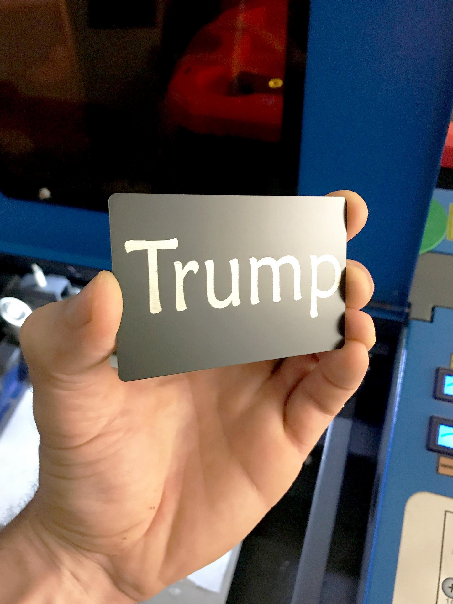 Hand holding a black metal card with 'Trump Card' printed on it in front of a colorful background.