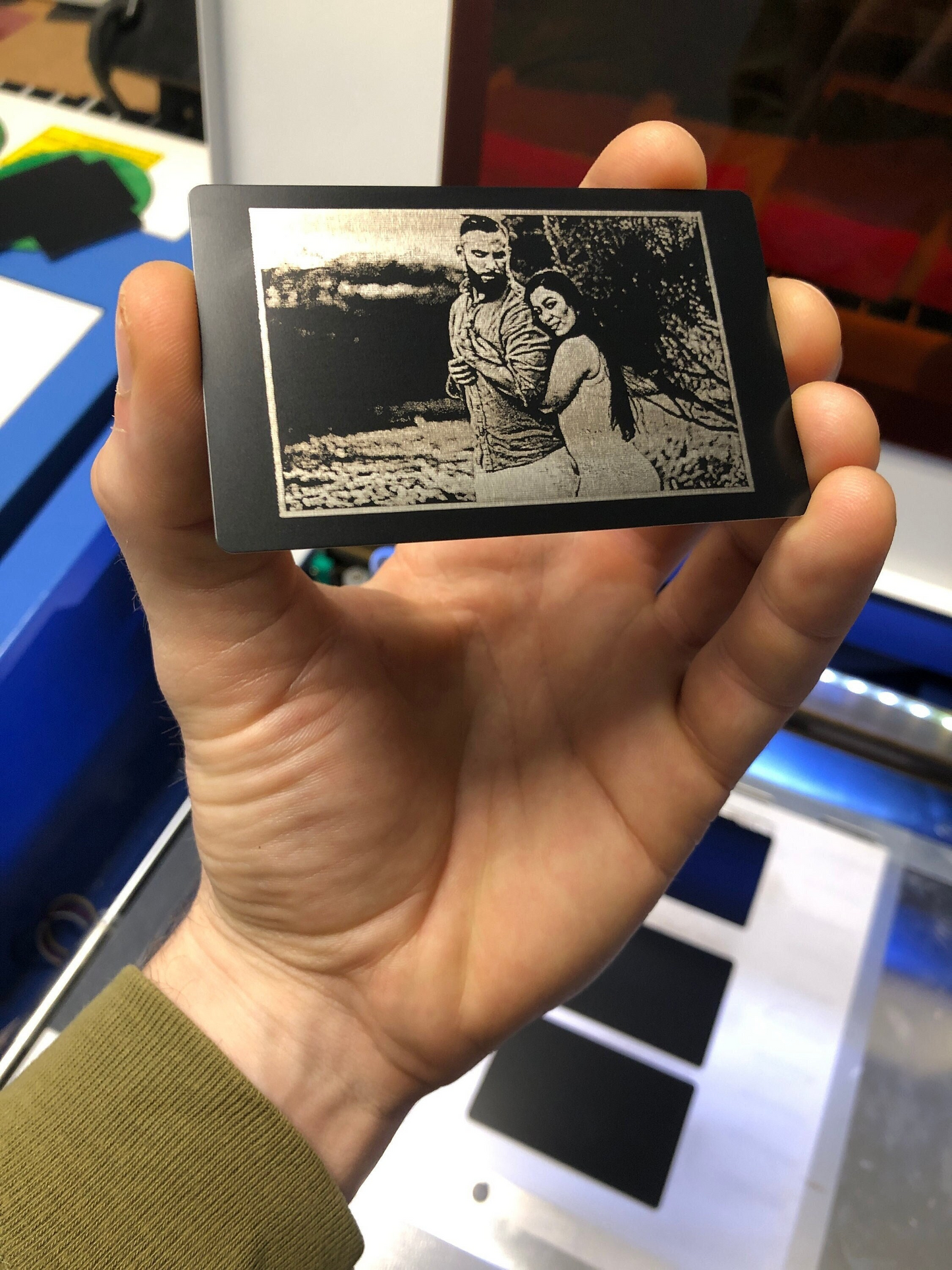 Hand holding a small rectangular device displaying a personalized engagement photo