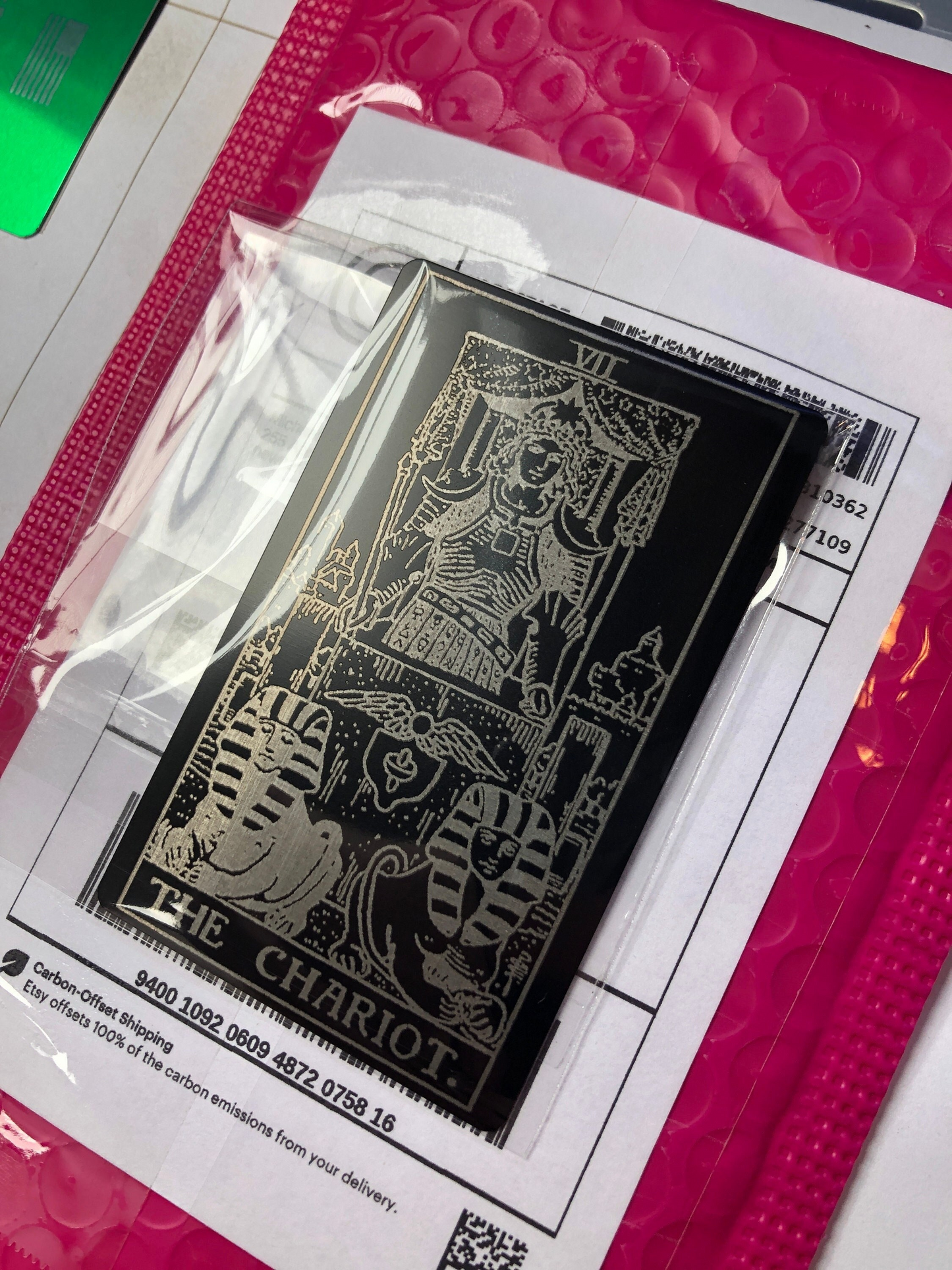 Black and silver metal tarot card of 'The Chariot' on a pink cutting mat.