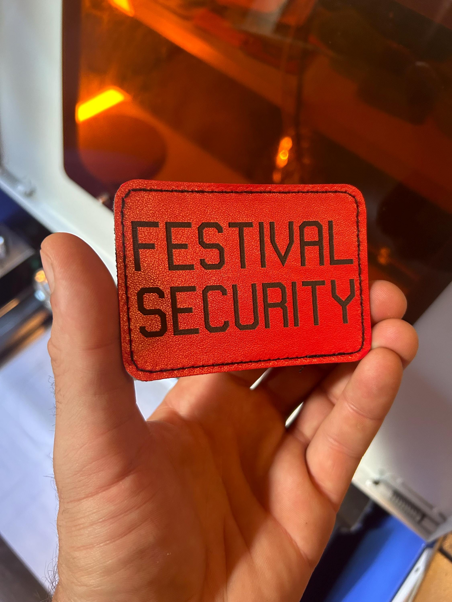 Red 'Festival Security' leather patch held in a hand with a blurred background