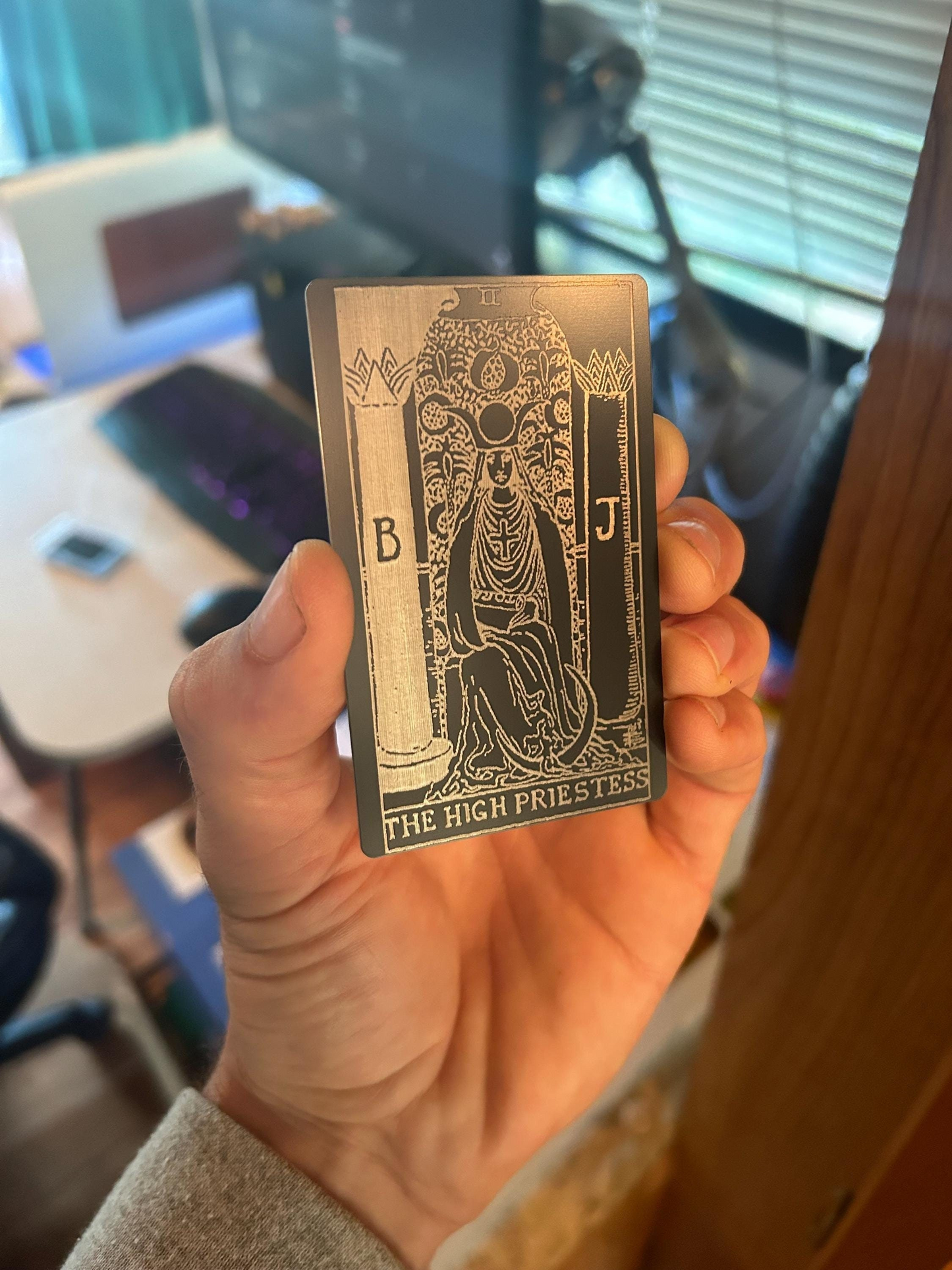 Hand holding a metal tarot card with intricate design and text.