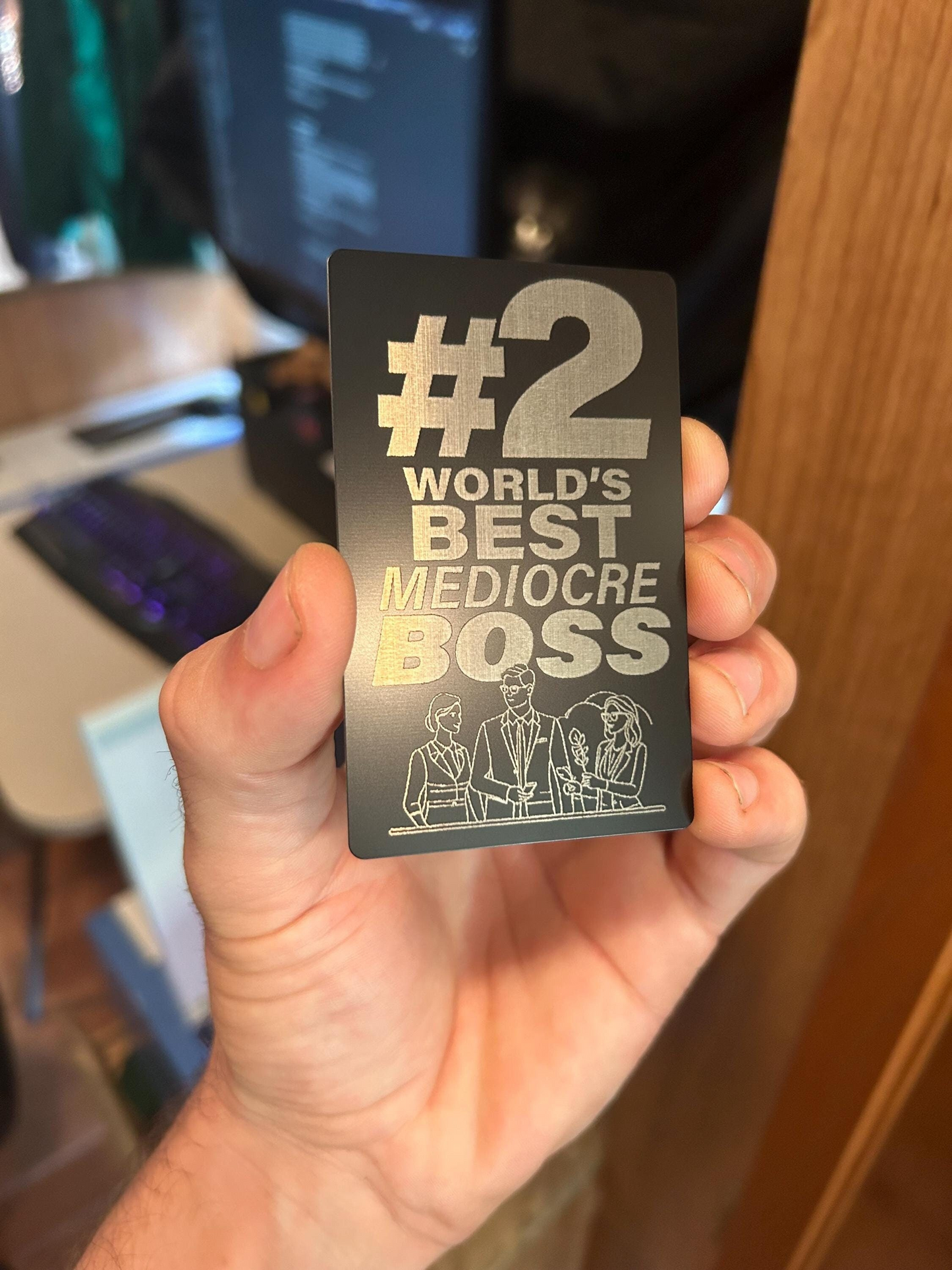 Hand holding a card with '#2 World's Best Mediocre Boss' text and illustration.