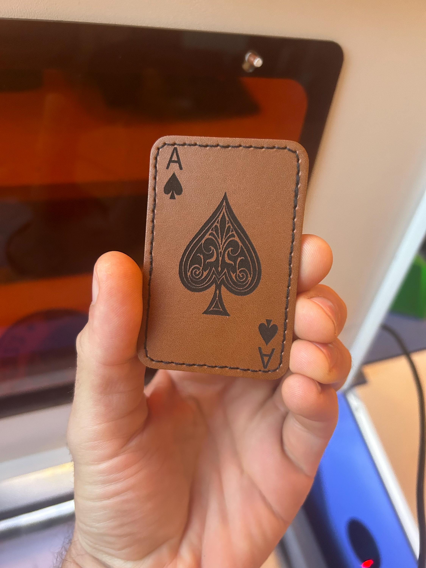 Hand holding a brown leather heat transfer patch with an Ace of Spades design.