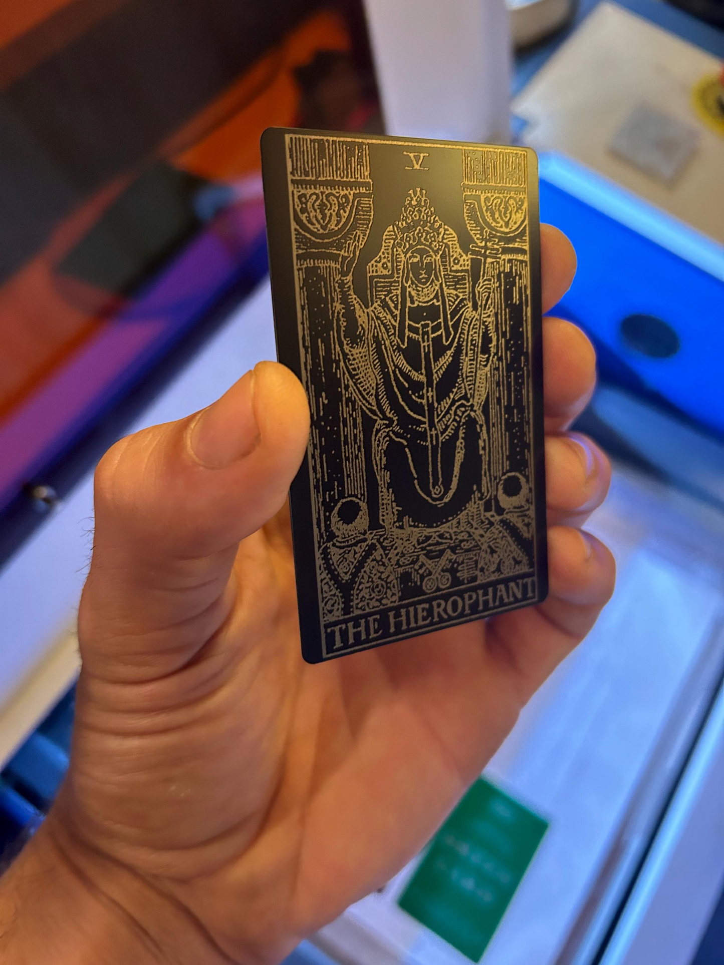 Hand holding a metal The Hierophant tarot card with intricate design and text laser engraved in anodized aluminum
