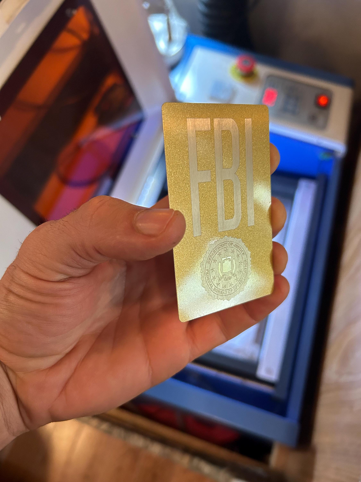 Hand holding a gold laser engraved novelty badge gift card with customized logo branding in front of a blurred background