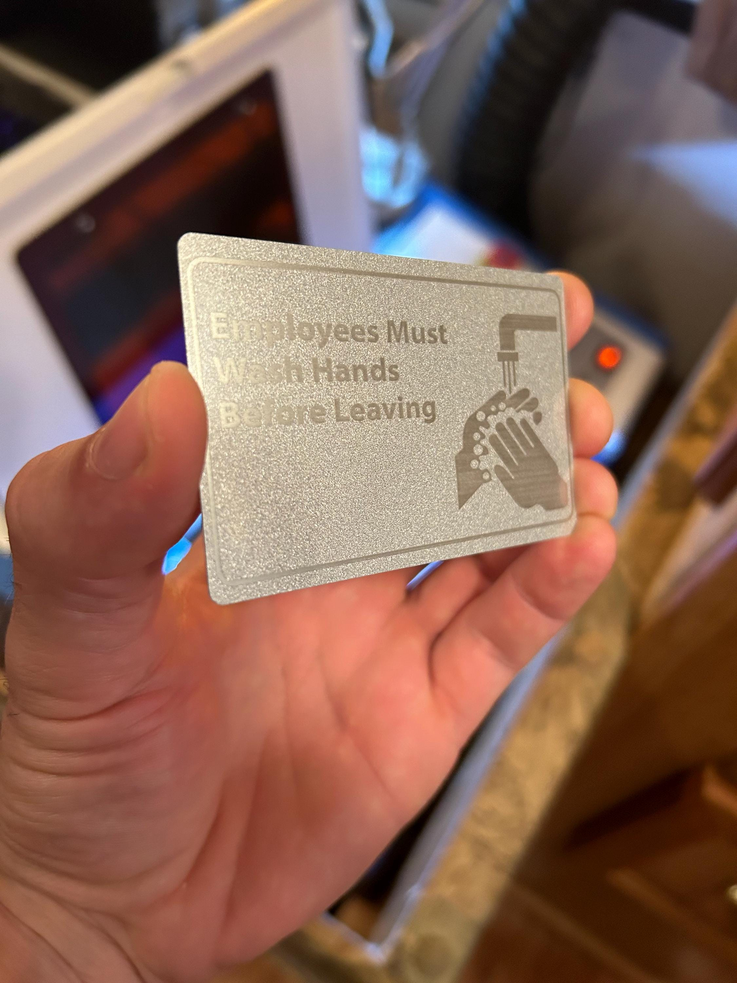 Metal sign with text 'Employees Must Wash Hands Before Leaving' held by a hand, laser engraved on a silver/silver anodized aluminum placard