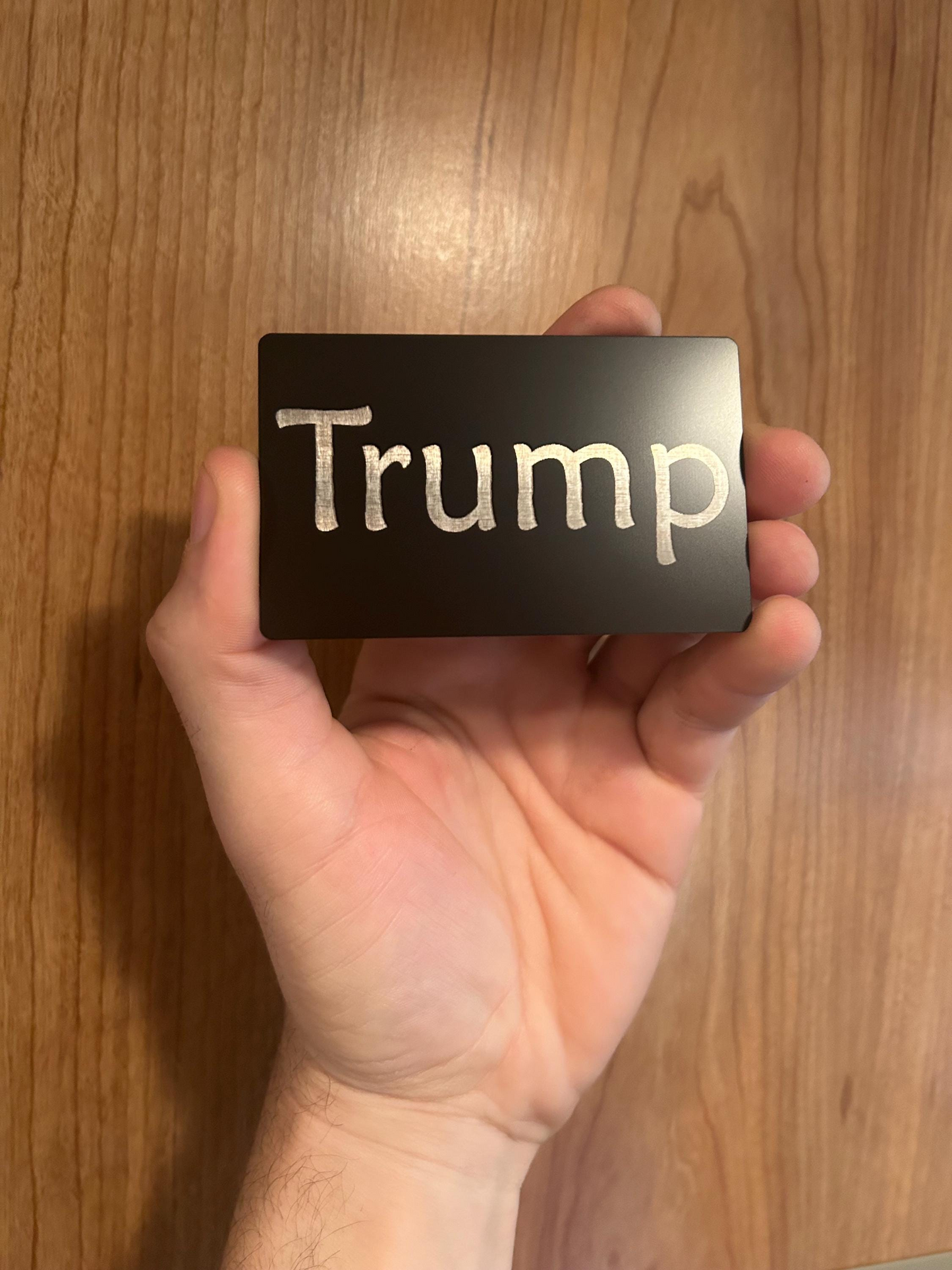 Hand holding a card with 'Trump' printed on it against a wooden background