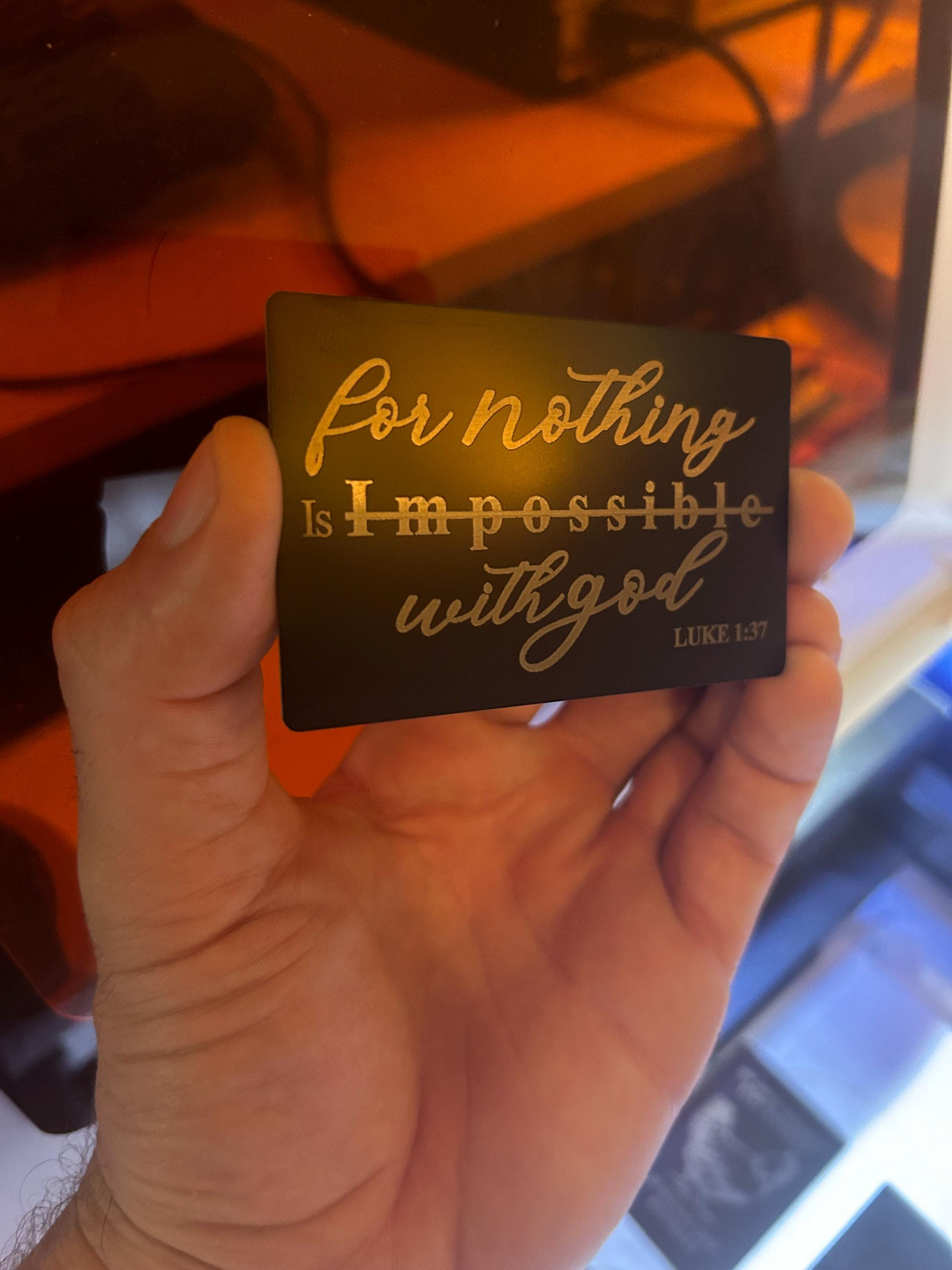 Hand holding a card with motivational quote 'For nothing is impossible with God' in silver text on a black background.