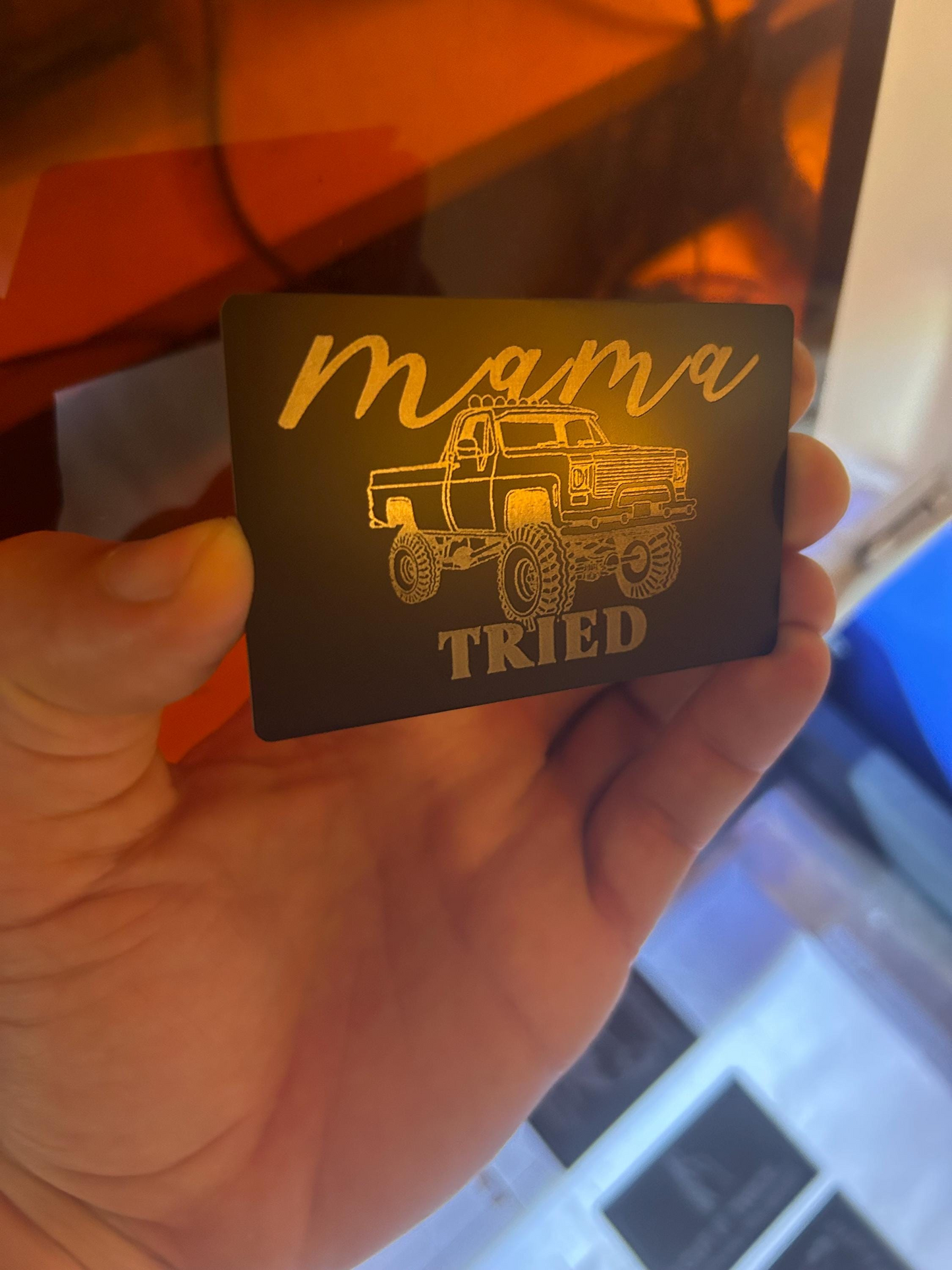 metal keepsake wallet insert with 'mama tried' text and lifted truck illustration held by a hand.