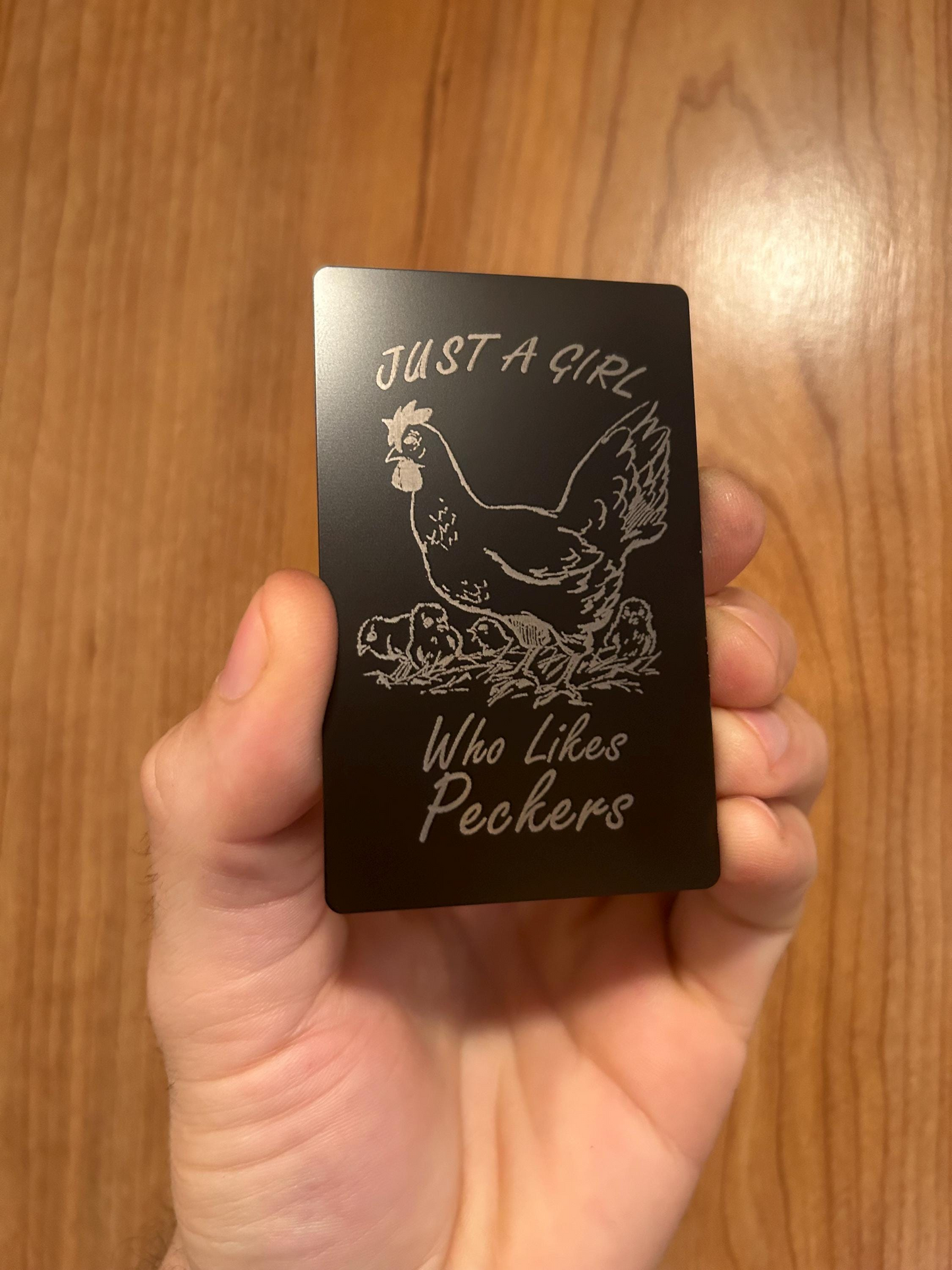 Detailed view of laser cut gag gift card in black/silver anodized aluminum engraved with chicken artwork and joke text