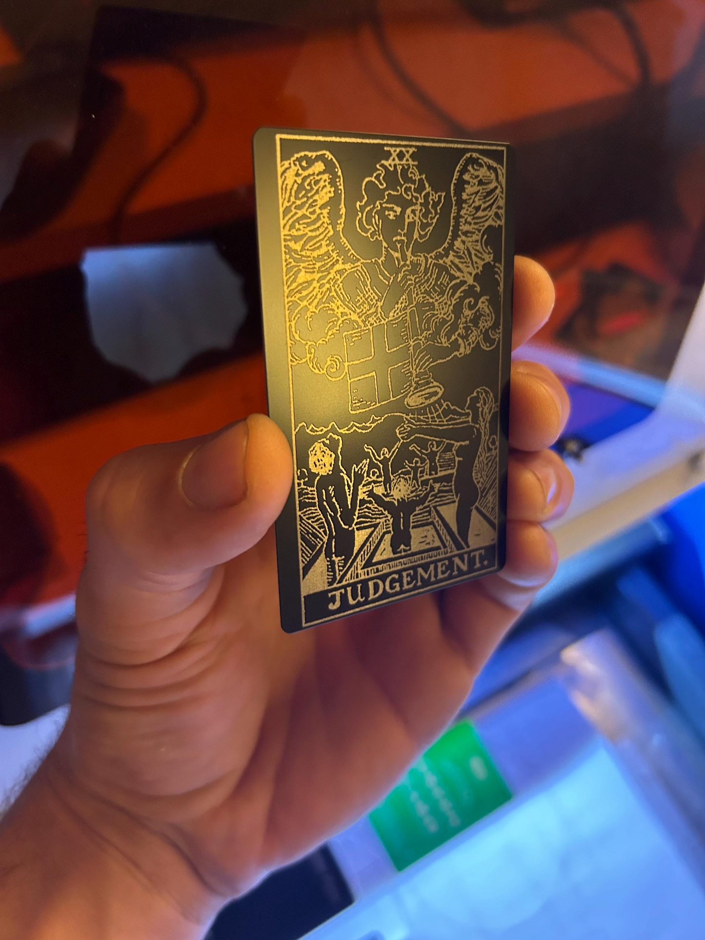 Hand holding a metal tarot card with intricate designs and 'Judgment' text.