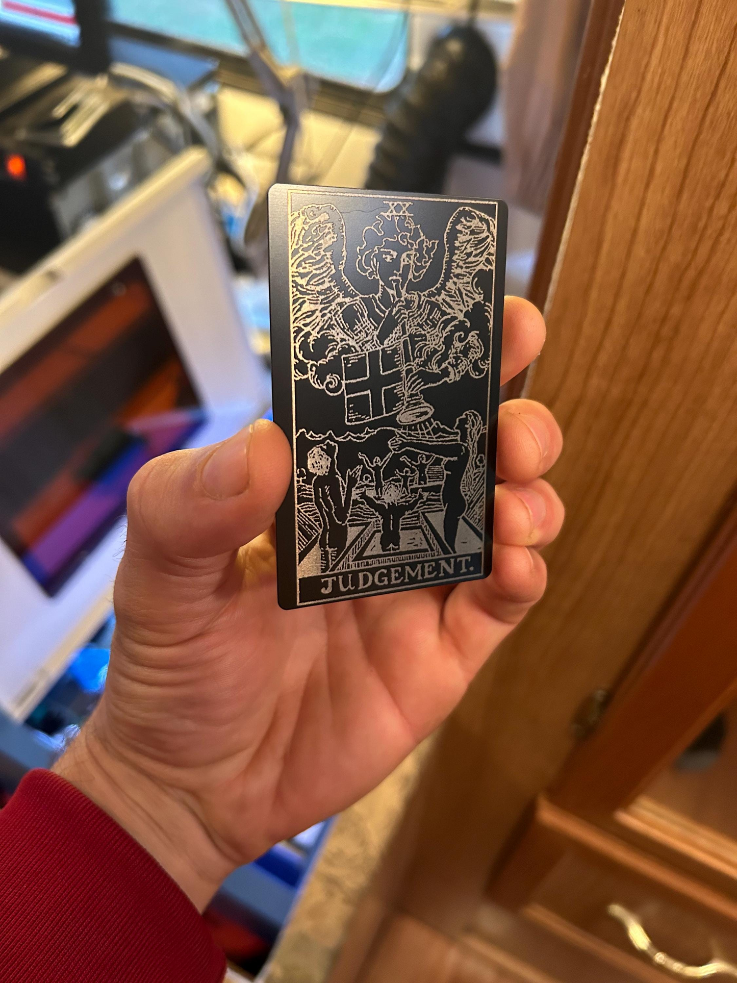 Hand holding a metal tarot card with intricate design and 'Judgement' text in an indoor setting.