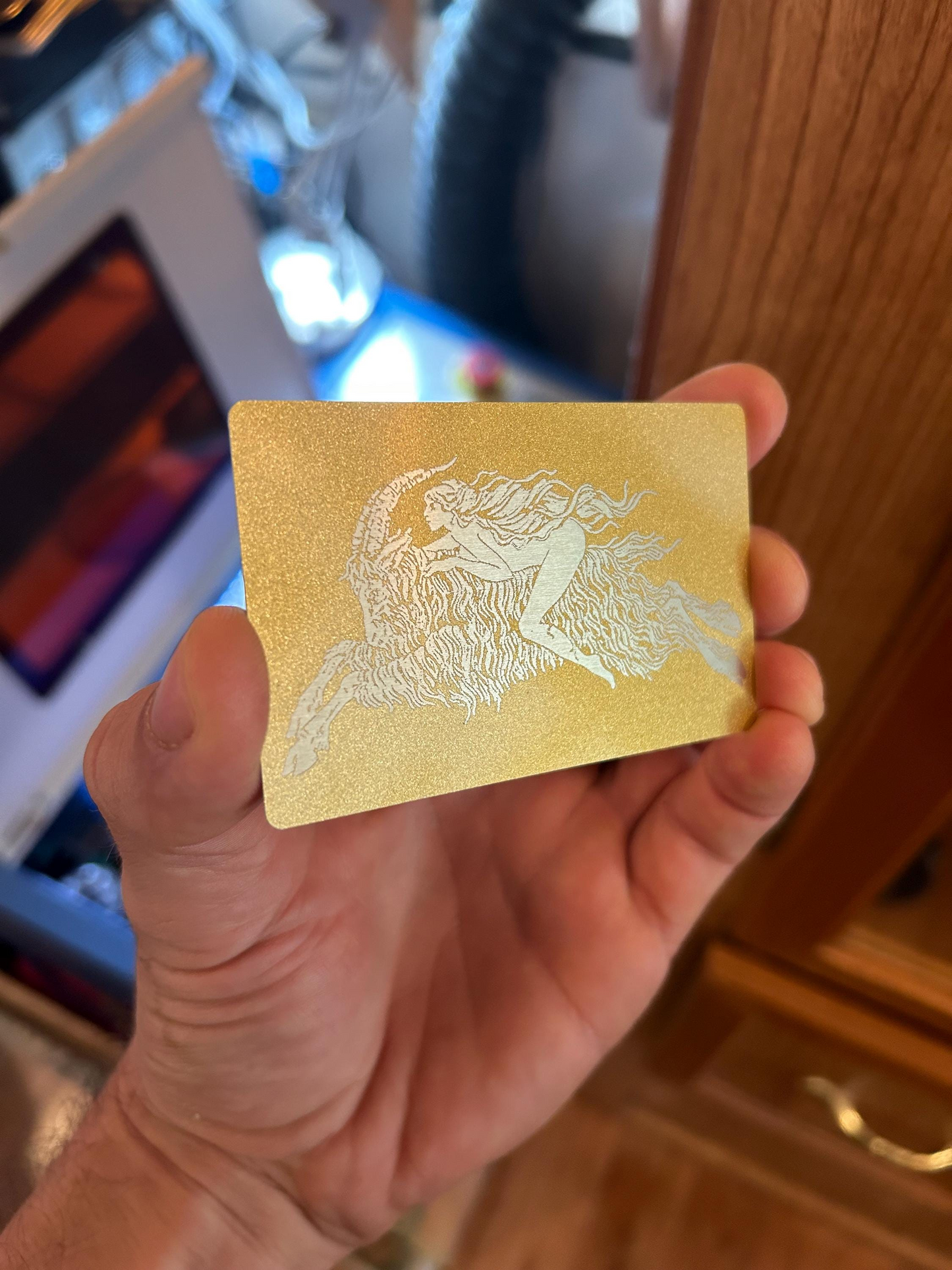 Hand holding a gold metal business card with a customized silver laser engraved design of a horse on a blurred background