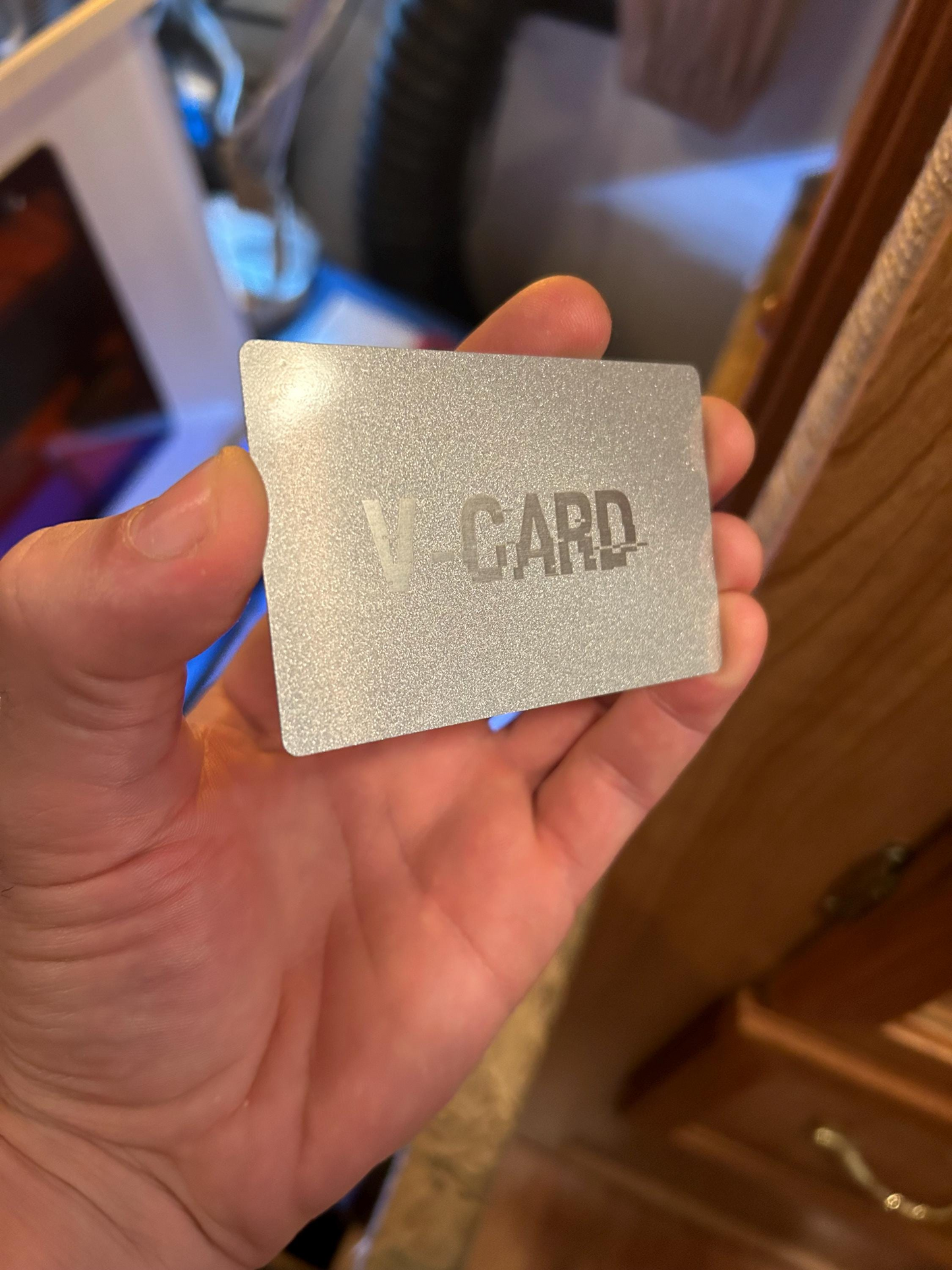 Hand holding a silver laser engraved metal business card with personalized engraving on it, blurred background