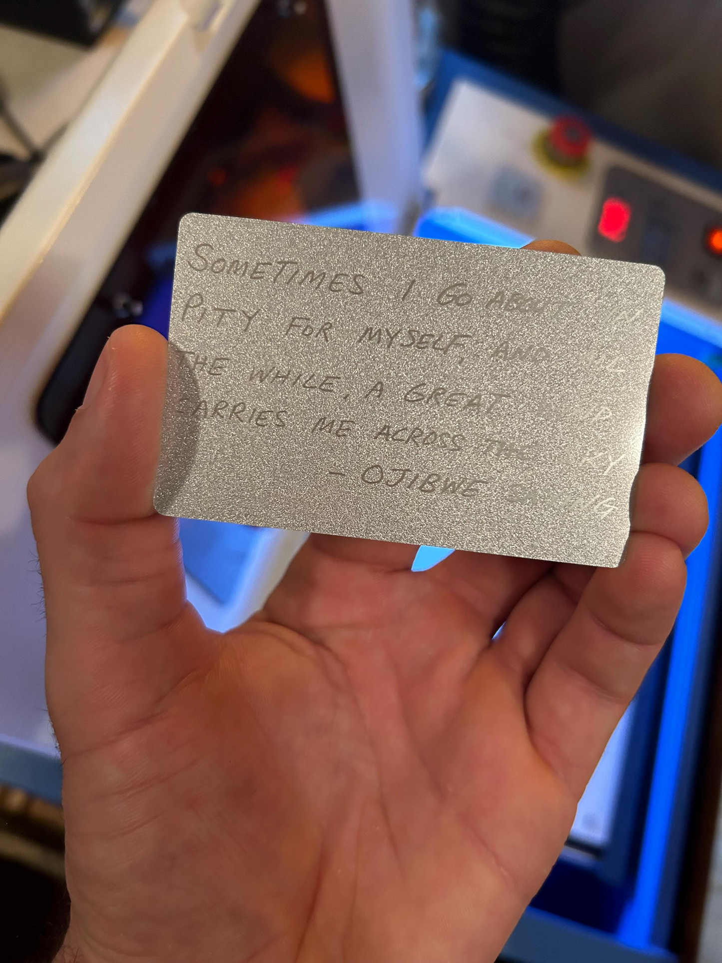 Hand holding a silver card with silver text in front of a machine.