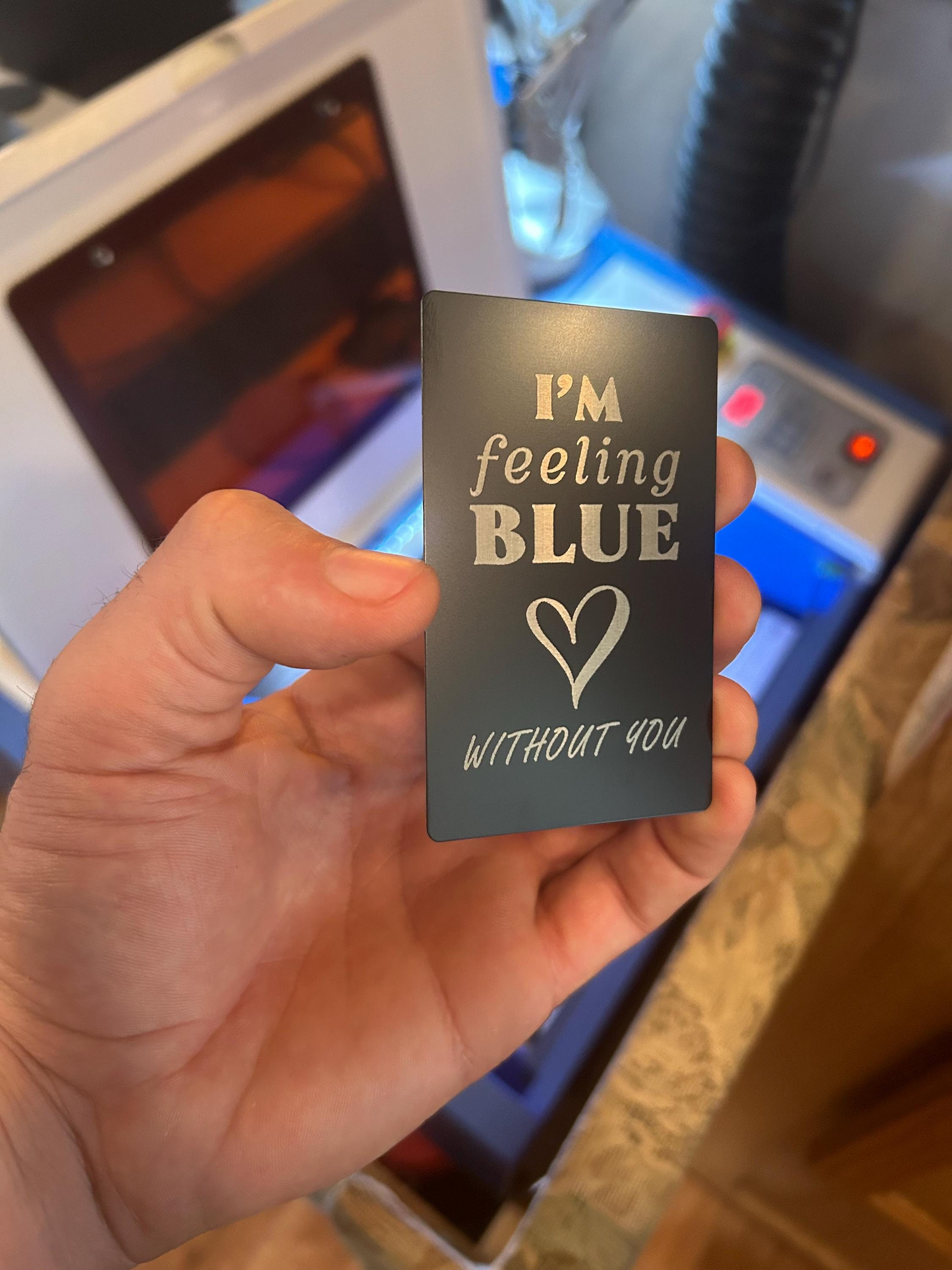 Hand holding a small metal black card with 'I'm feeling blue without you' text engraved