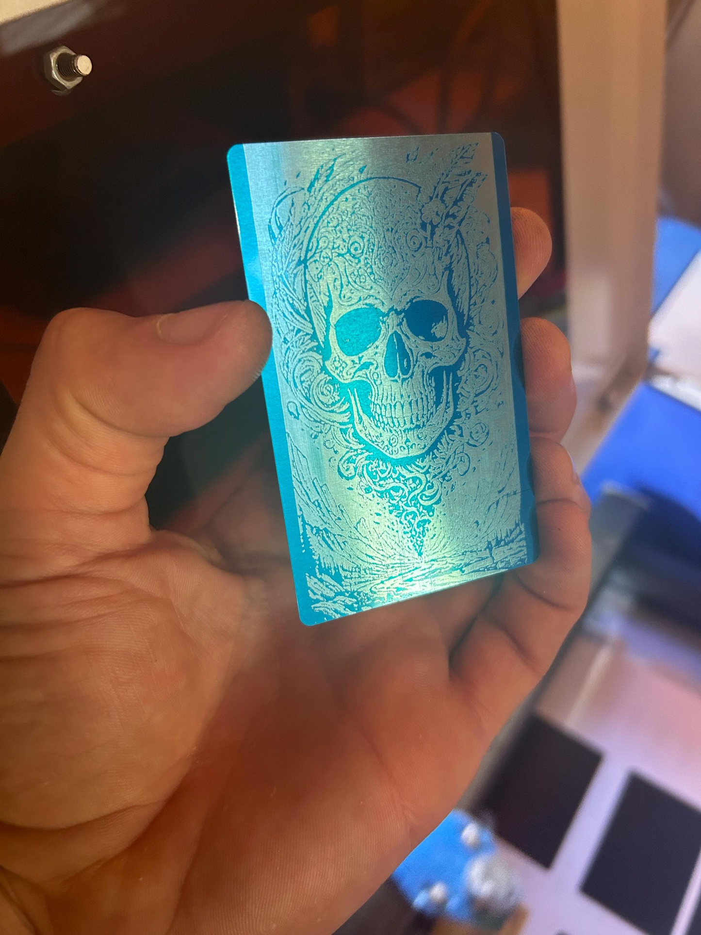 Hand holding a blue and silver metal illustration art card with skull design against a blurred background