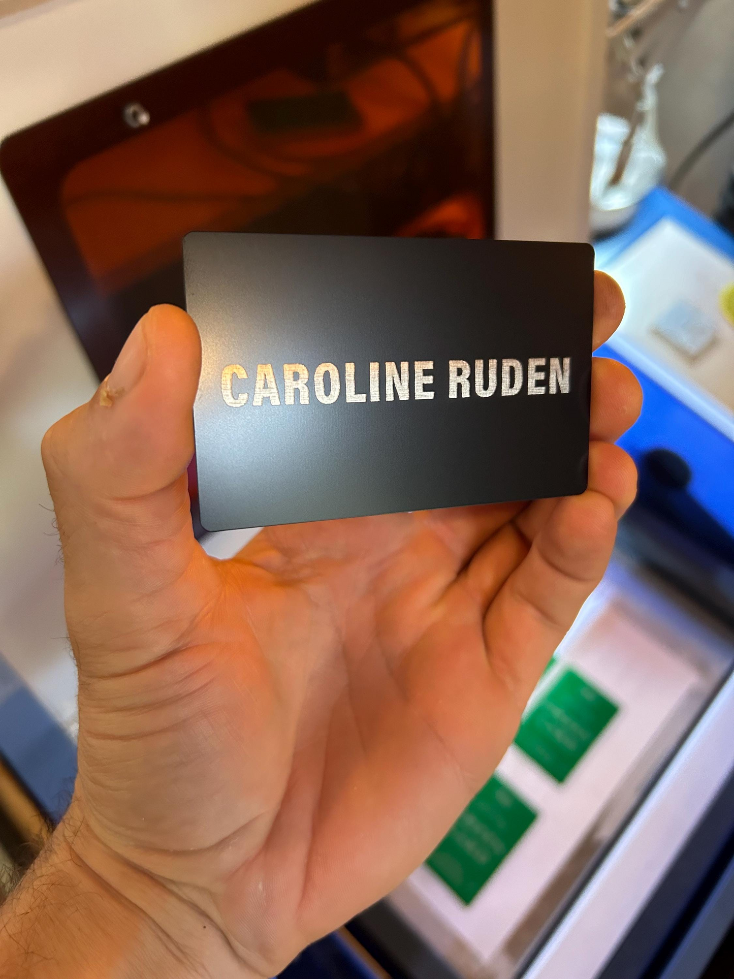 Hand holding a black card with custom name laser engraved on it, with a blurred background.