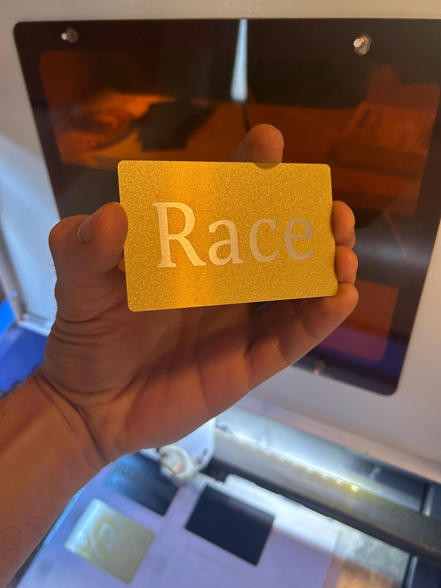 Hand holding a metal gold card with 'Race' printed on it in front of a reflective surface.