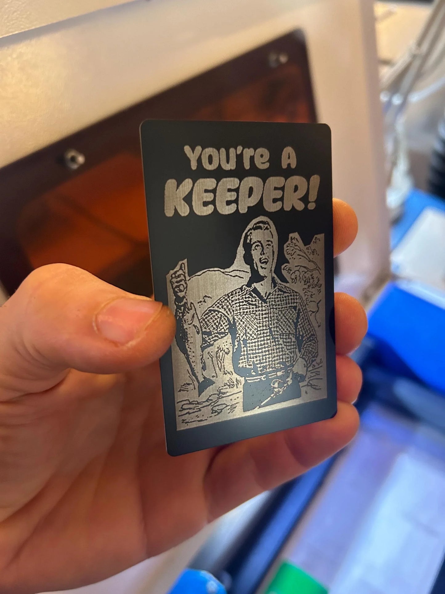 Hand holding a small card with 'You're a Keeper!' text and illustration.