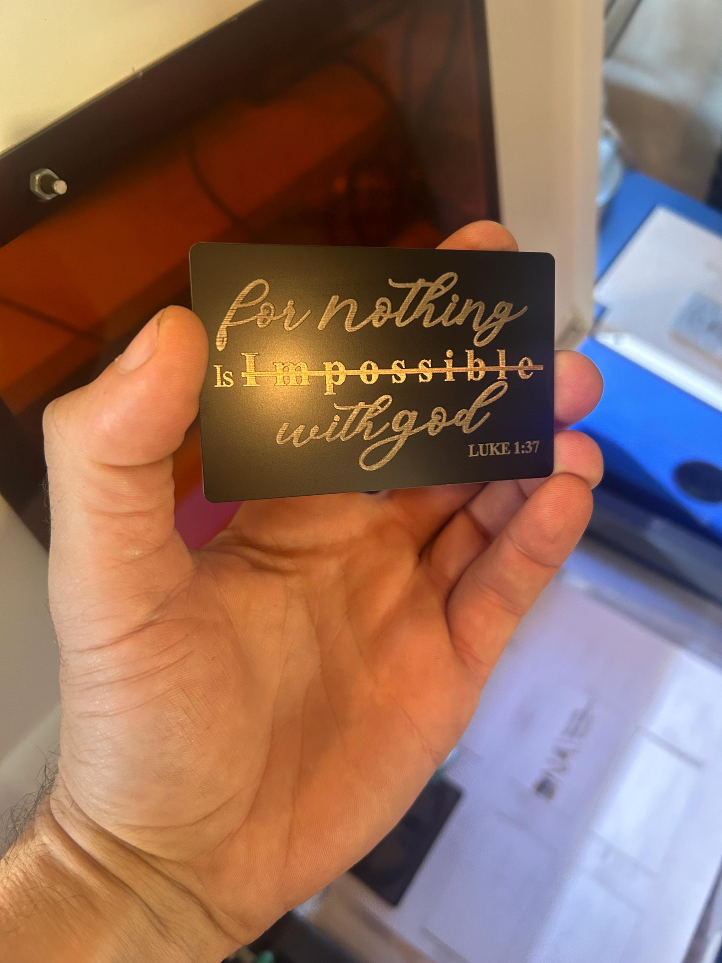 Hand holding a black card with engraved text 'For nothing is impossible with God' from Luke 1:37.