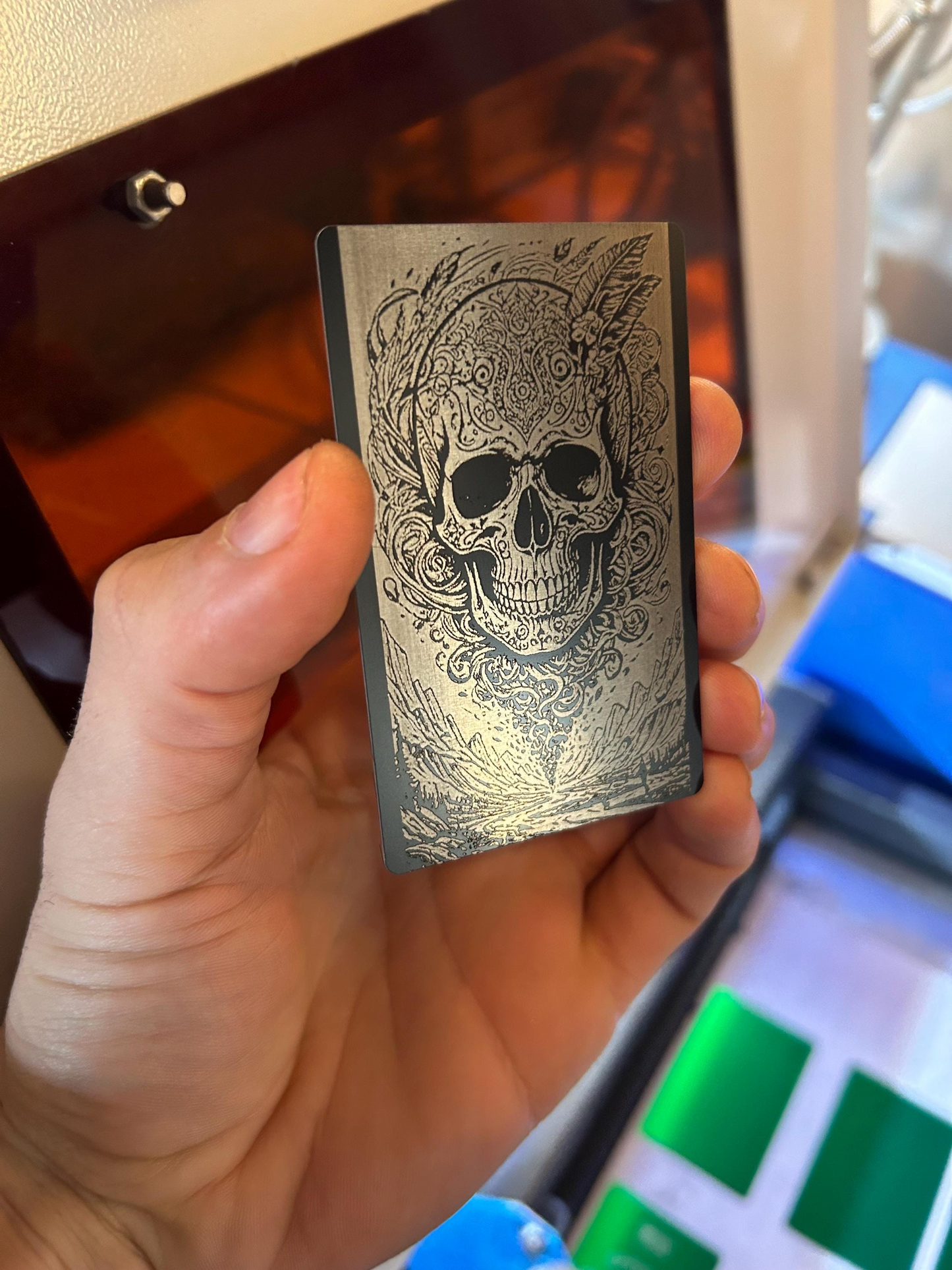 Hand holding a metallic wallet insert card with a psychedelic skull design against a blurred indoor background