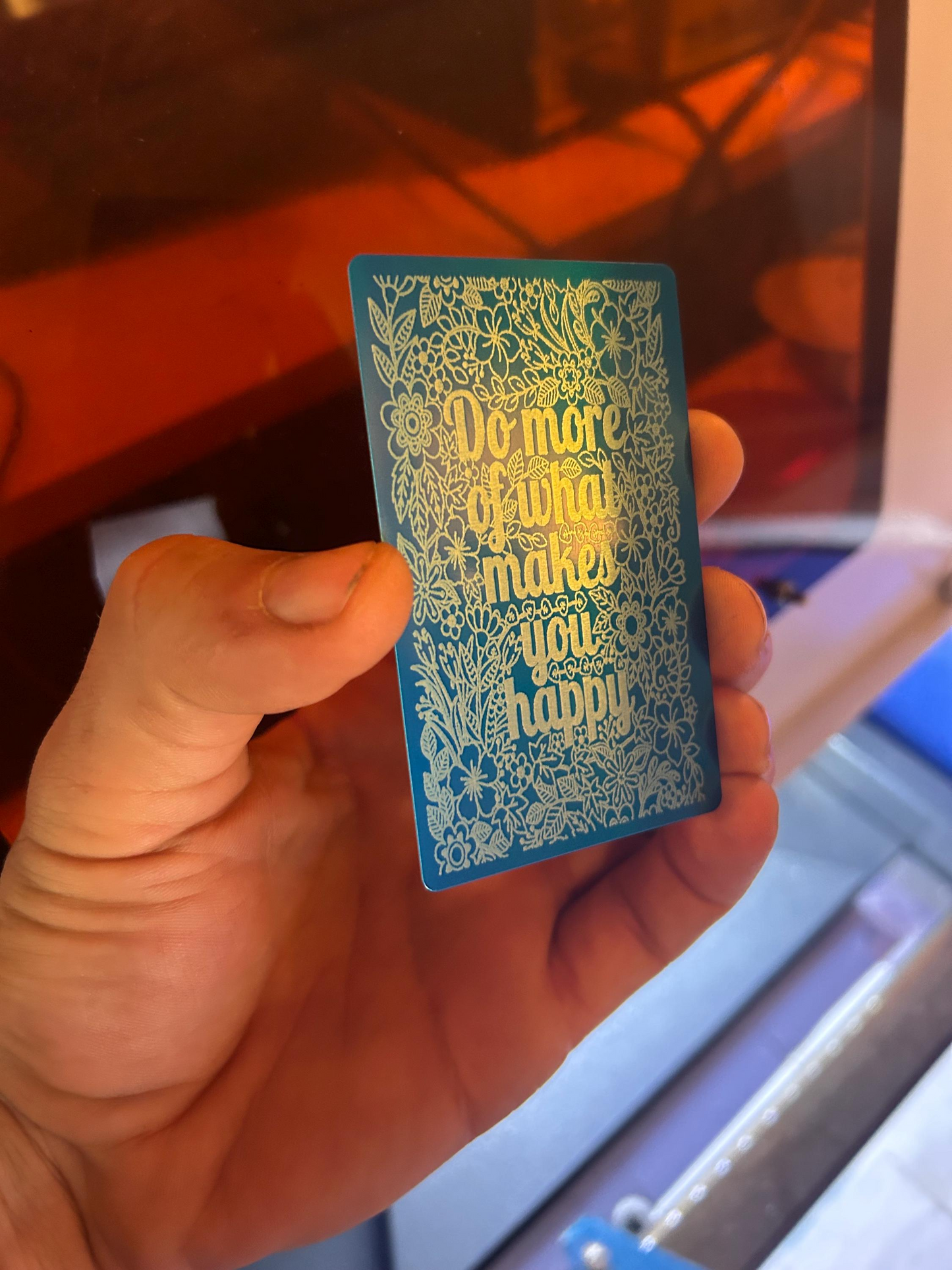 Hand holding a blue metal inspirational card with silver motivational text against a blurred background