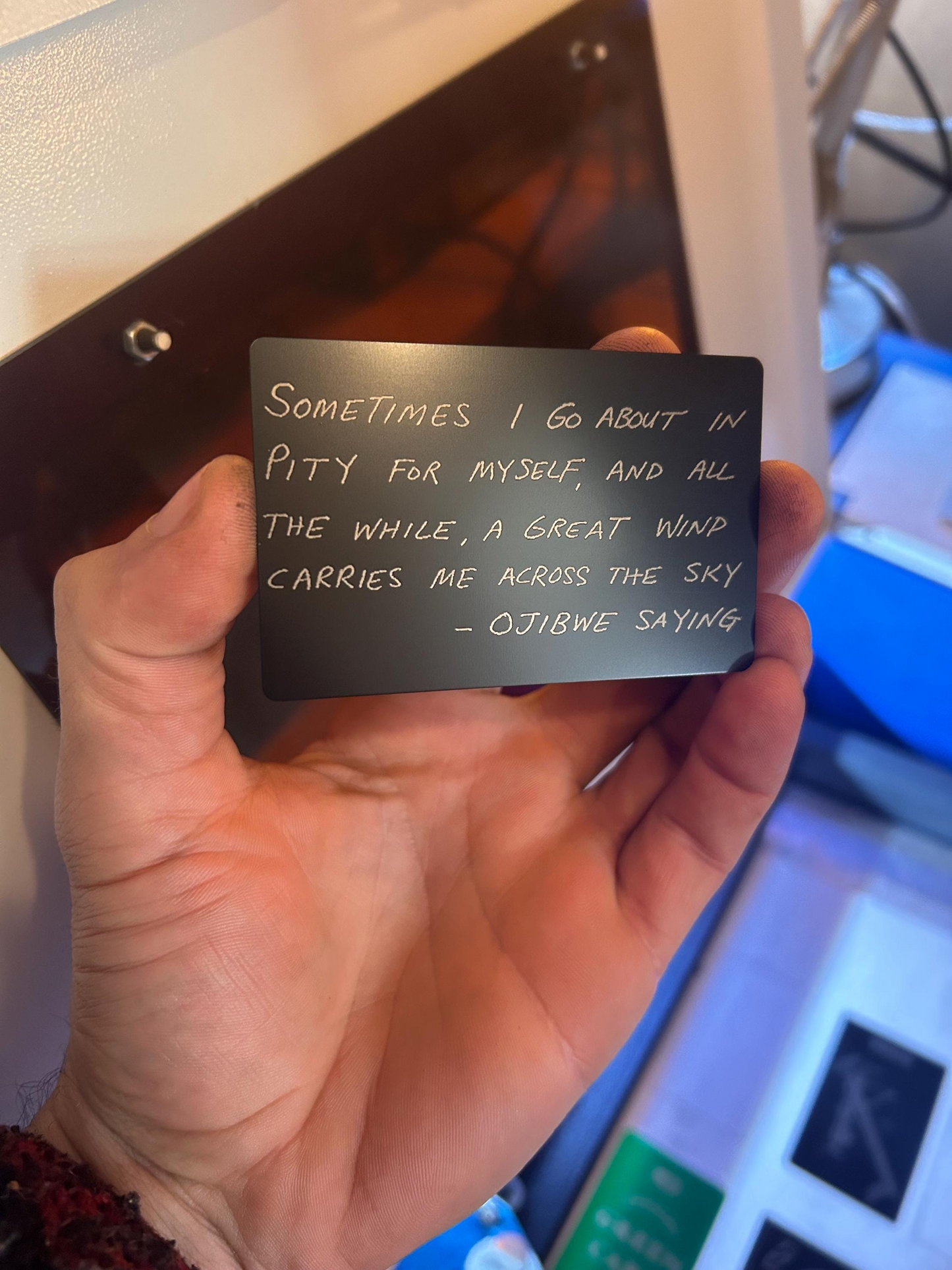 Hand holding a black card with handwritten ojibwe quote text engraved in an indoor setting