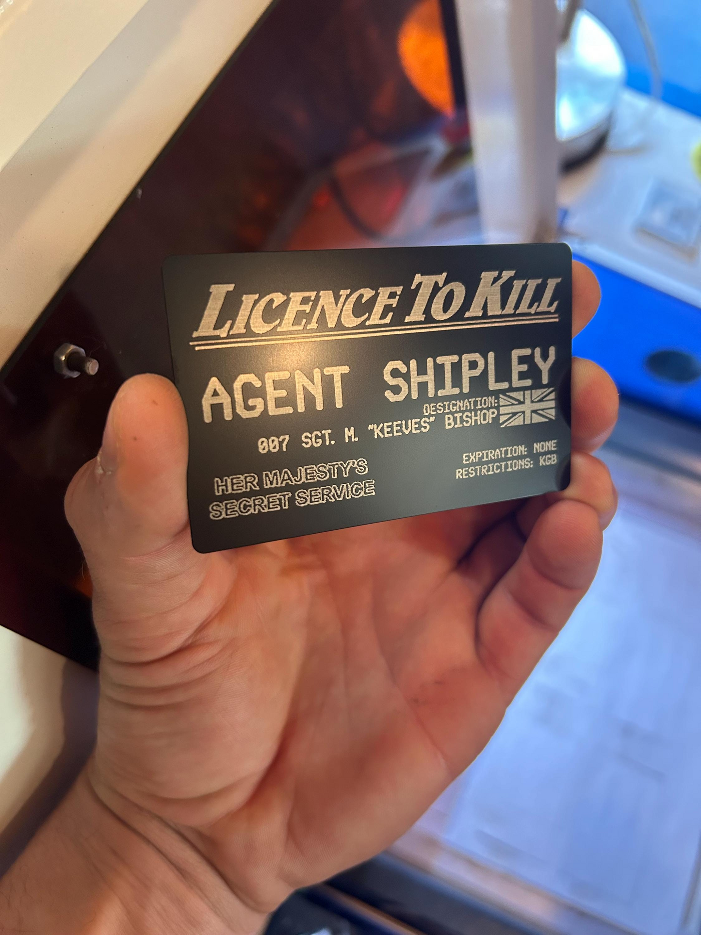 Black/silver metal business card with 'License To Kill' text held in a hand