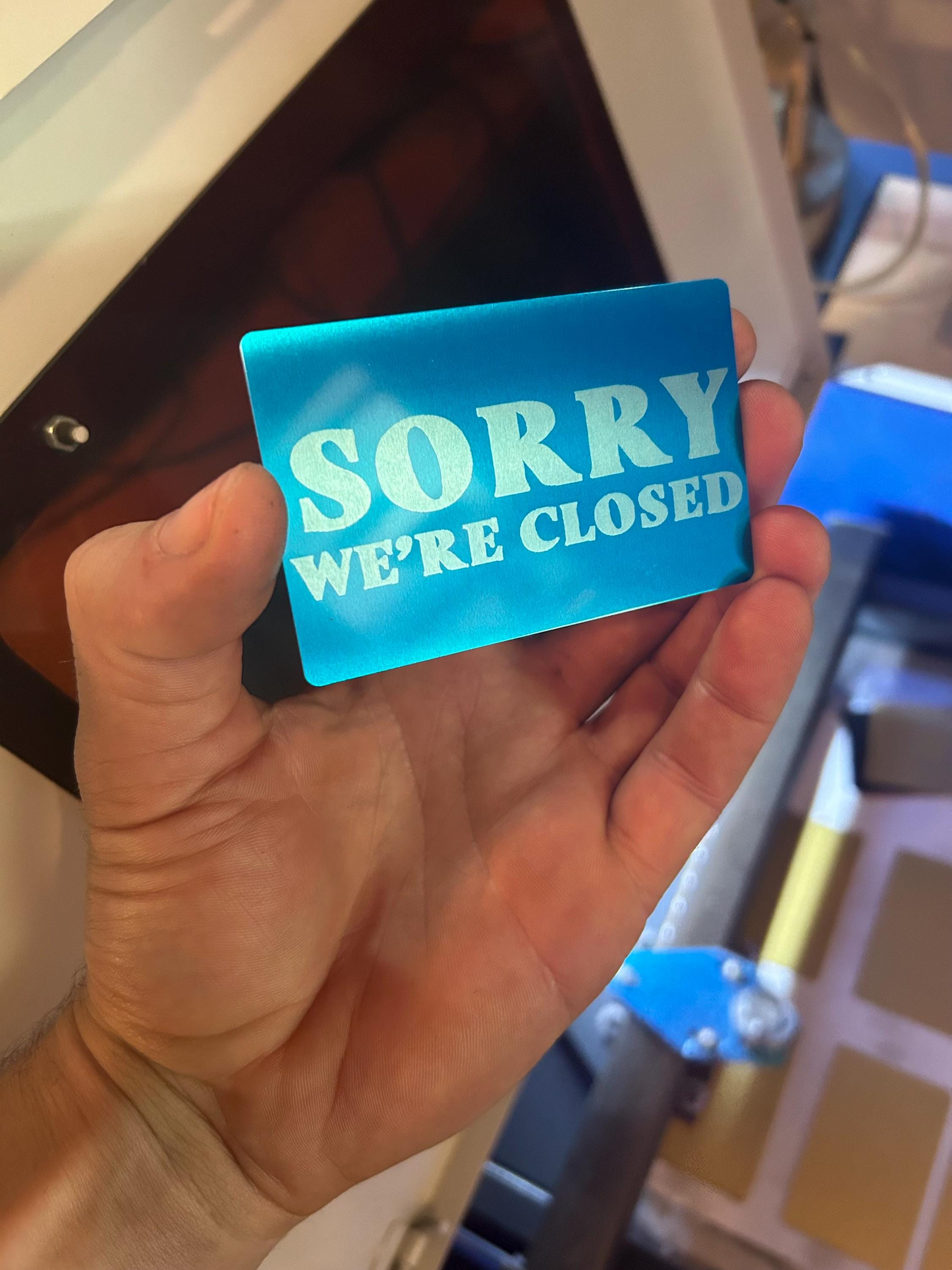 Hand holding a blue metal signage with 'Sorry We're Closed' text