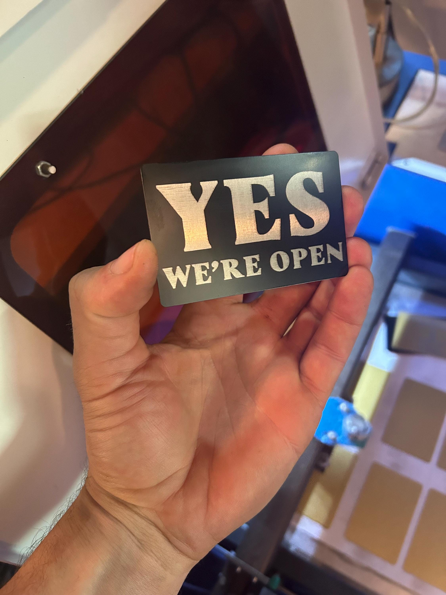 Hand holding a sign that says 'YES WE'RE OPEN' in front of a store entrance.